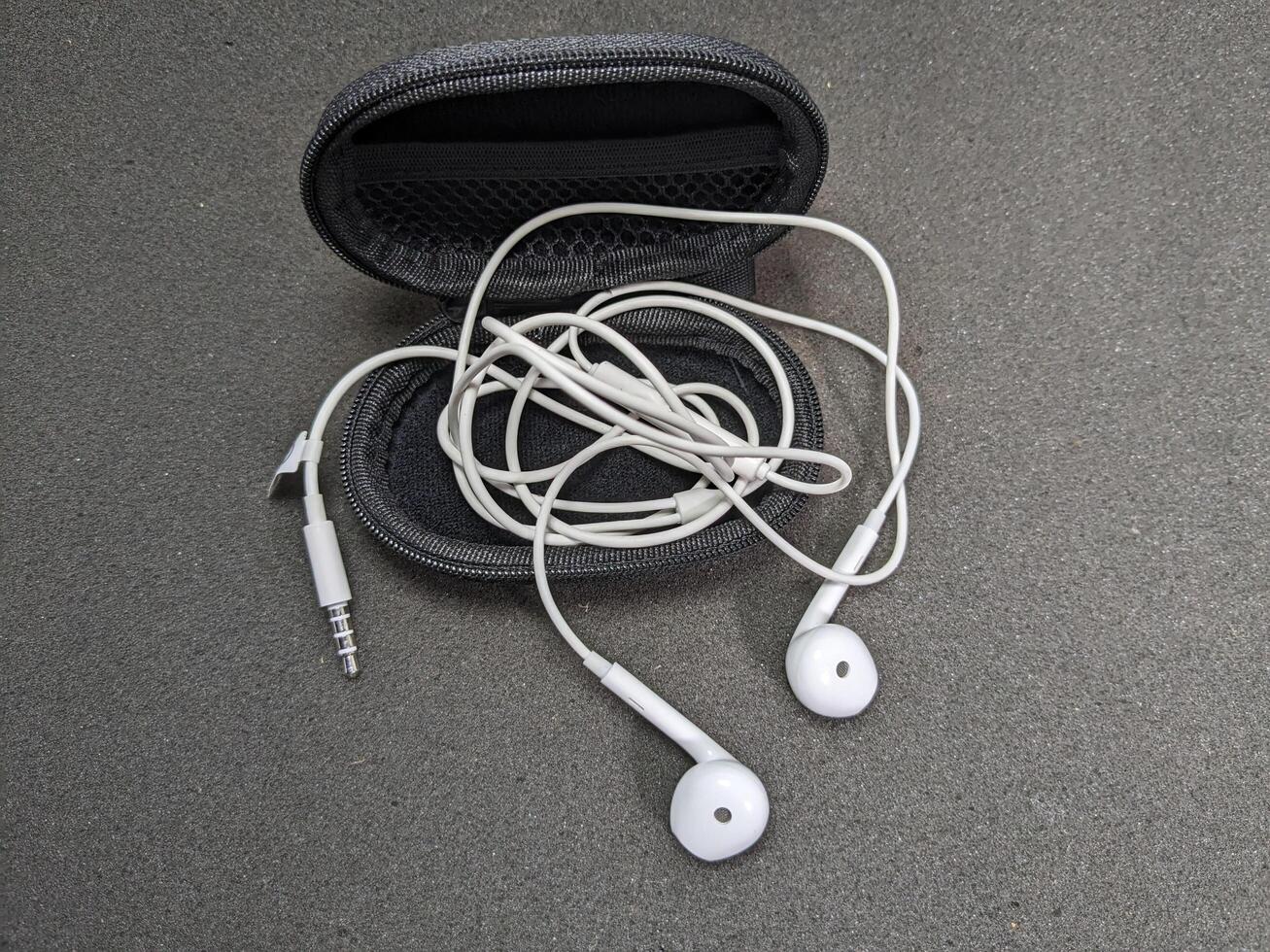 White Earphones and Black Case on Gray Surface, Isolated Overhead View photo