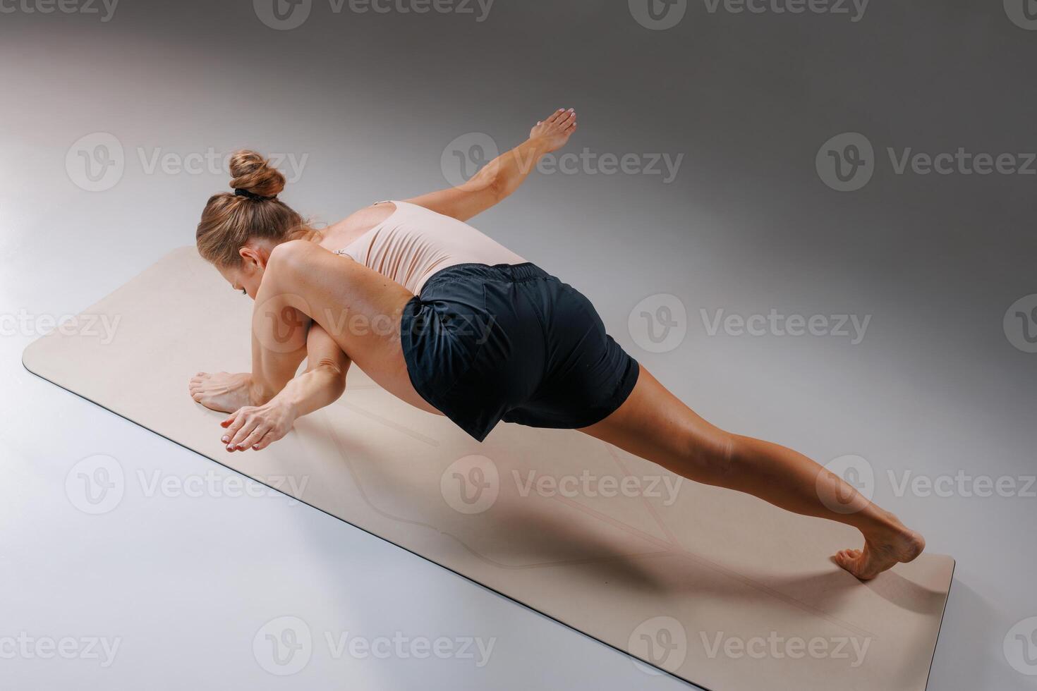 Woman practicing advanced yoga arm balance pose Eka Pada Koundinyasana on mat in studio, demonstrating core strength, balance, and flexibility in athletic wear. photo