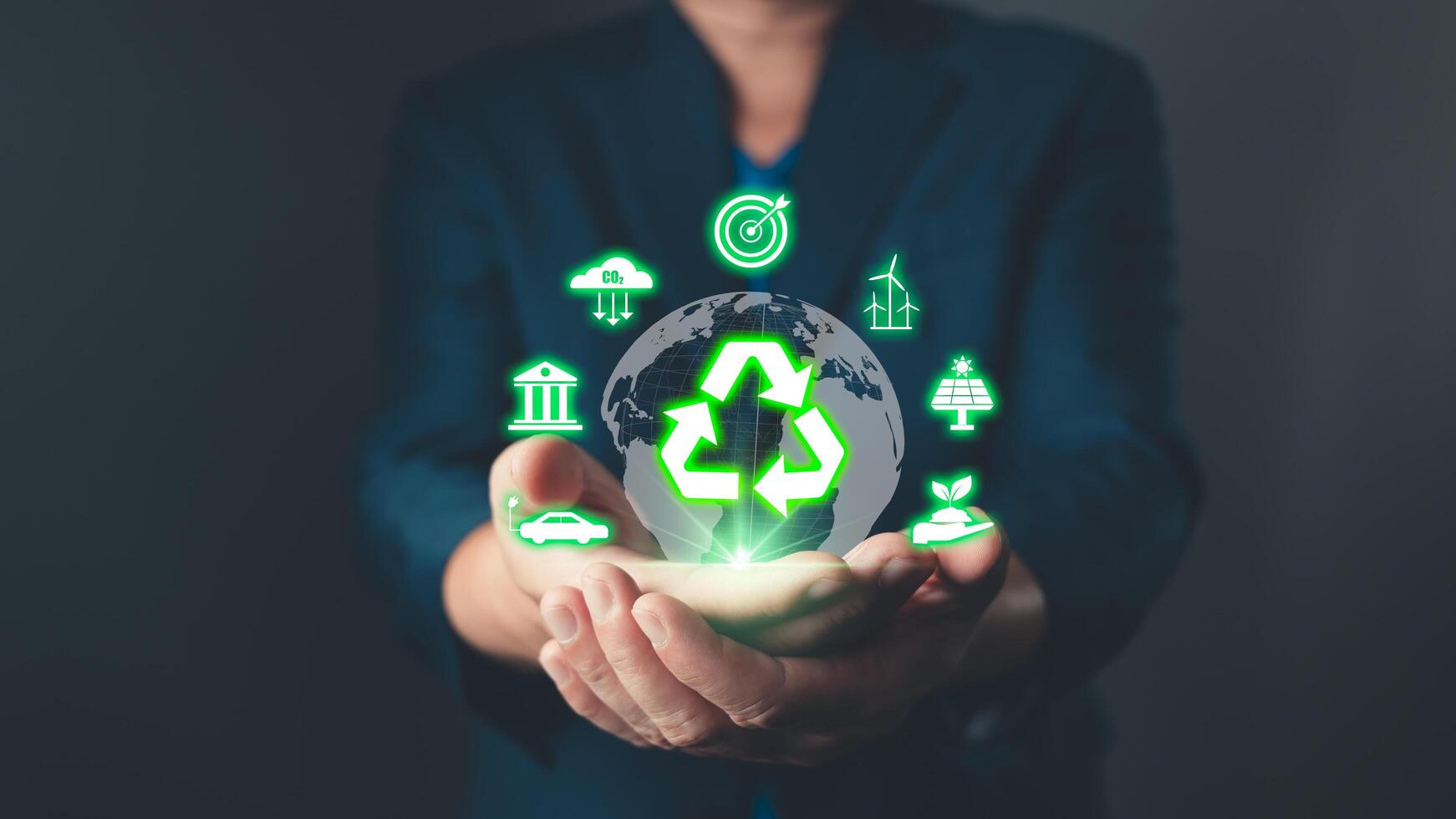 A person holds a glowing recycling symbol over a globe, surrounded by icons representing renewable energy, eco-friendly solutions, and sustainability. photo
