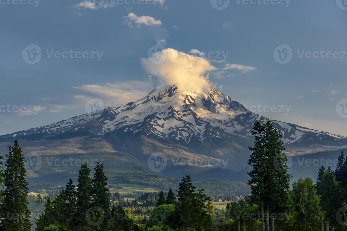 Majestic mountain peak with snow and cloud formations in a serene landscape during early evening hours photo