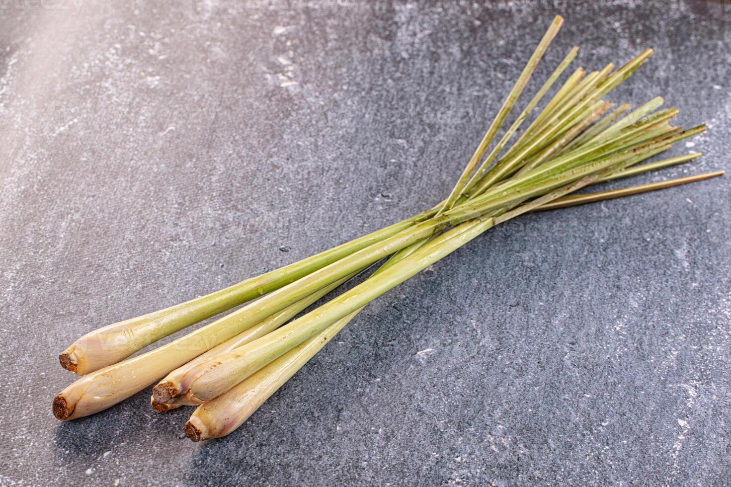 Three long, green stalks of lemongrass on a stone surface photo