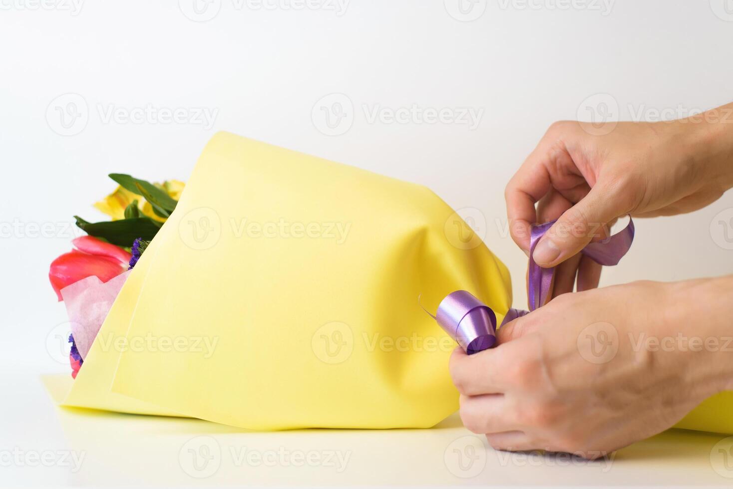 Florist decorating bouquet, close-up. Hands tying ribbon on bouquet of flowers indoors on white background, selective focus photo
