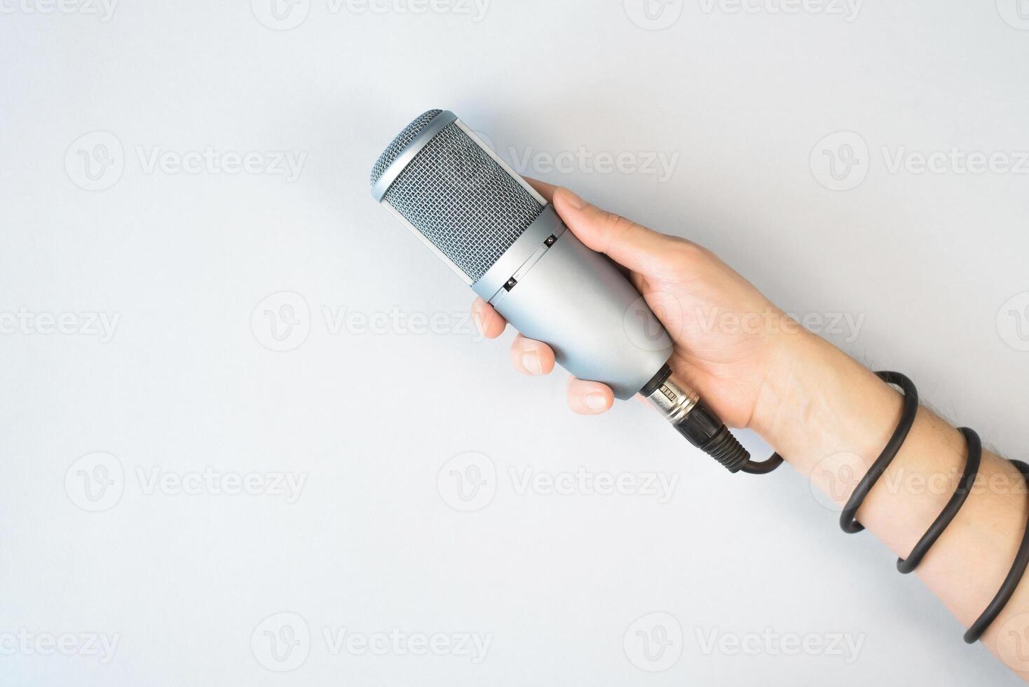 Male hand holding studio microphone, top view, light background. Cable is wrapped around the arm. Blogging, sound recording, podcast concept. photo