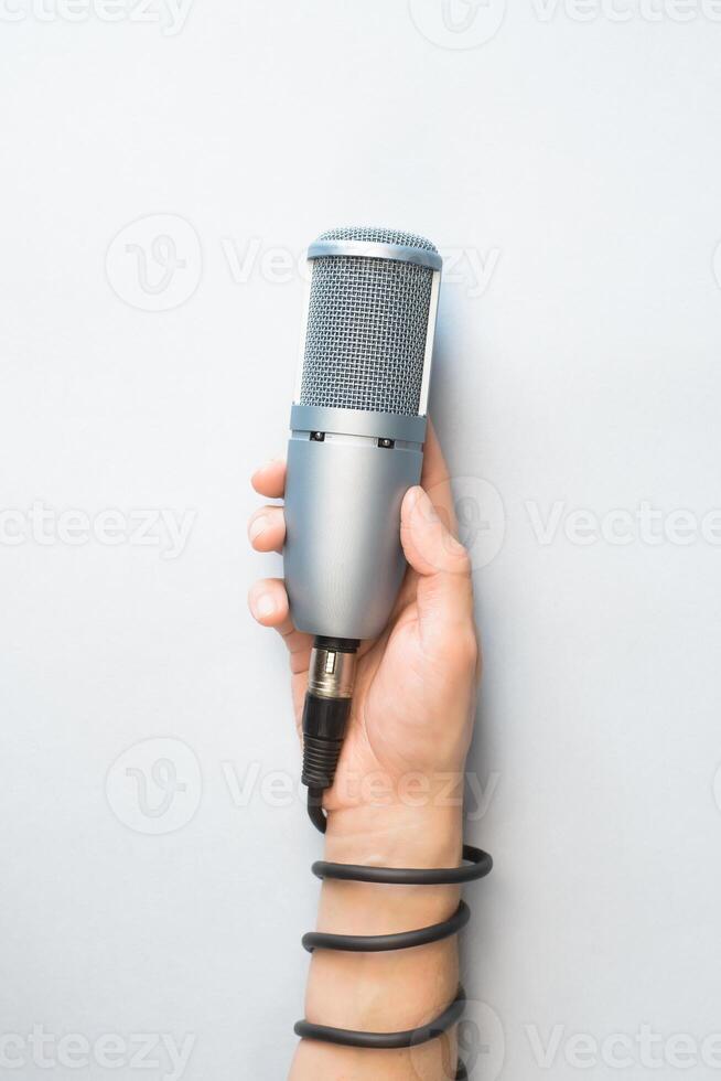 Male hand holding professional microphone on light background, top view. The microphone cable wrapped around hand. Vertical photo