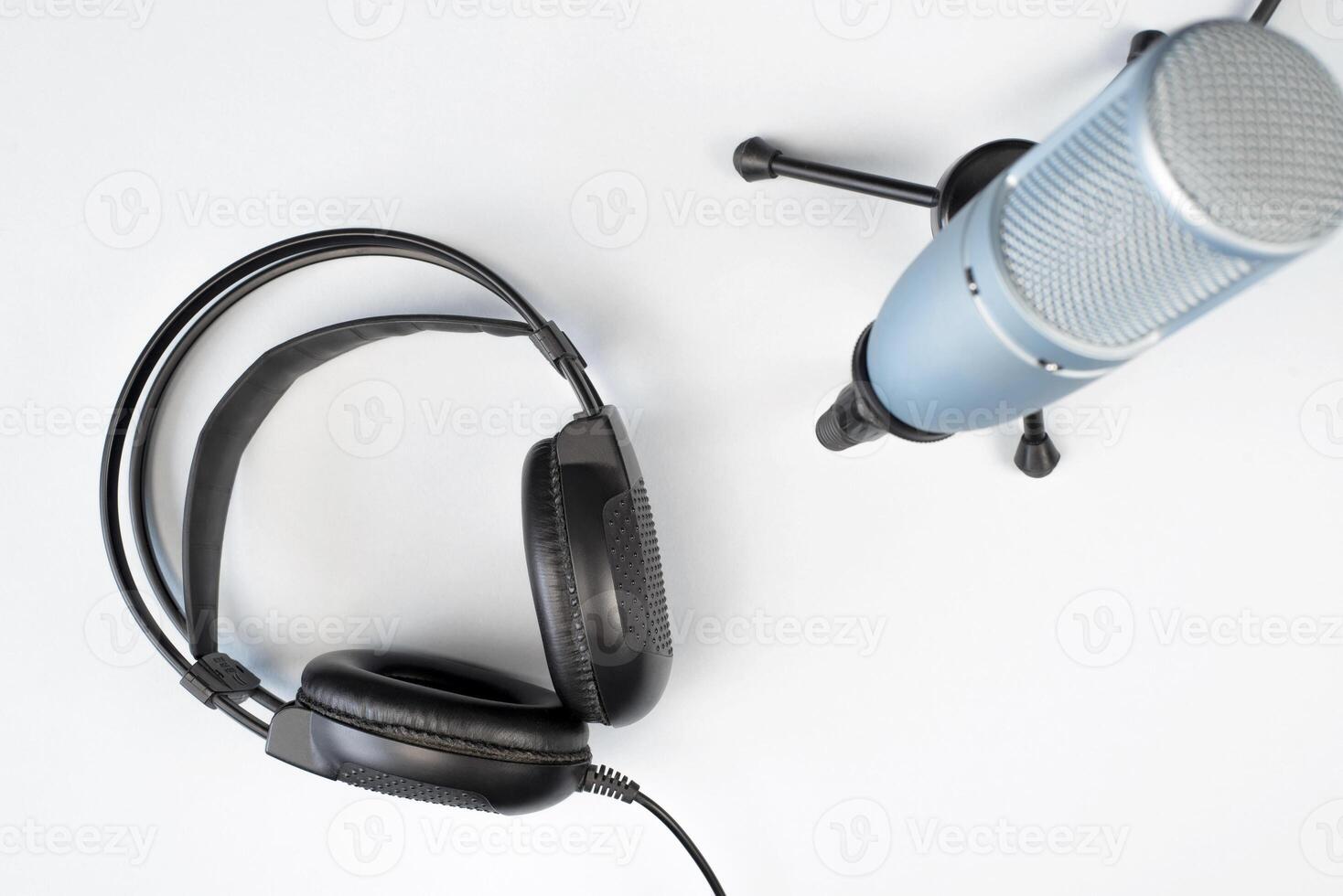Studio microphone on a stand and black headphones on a light background, top view. Professional equipment for online broadcasting. Podcast concept. photo