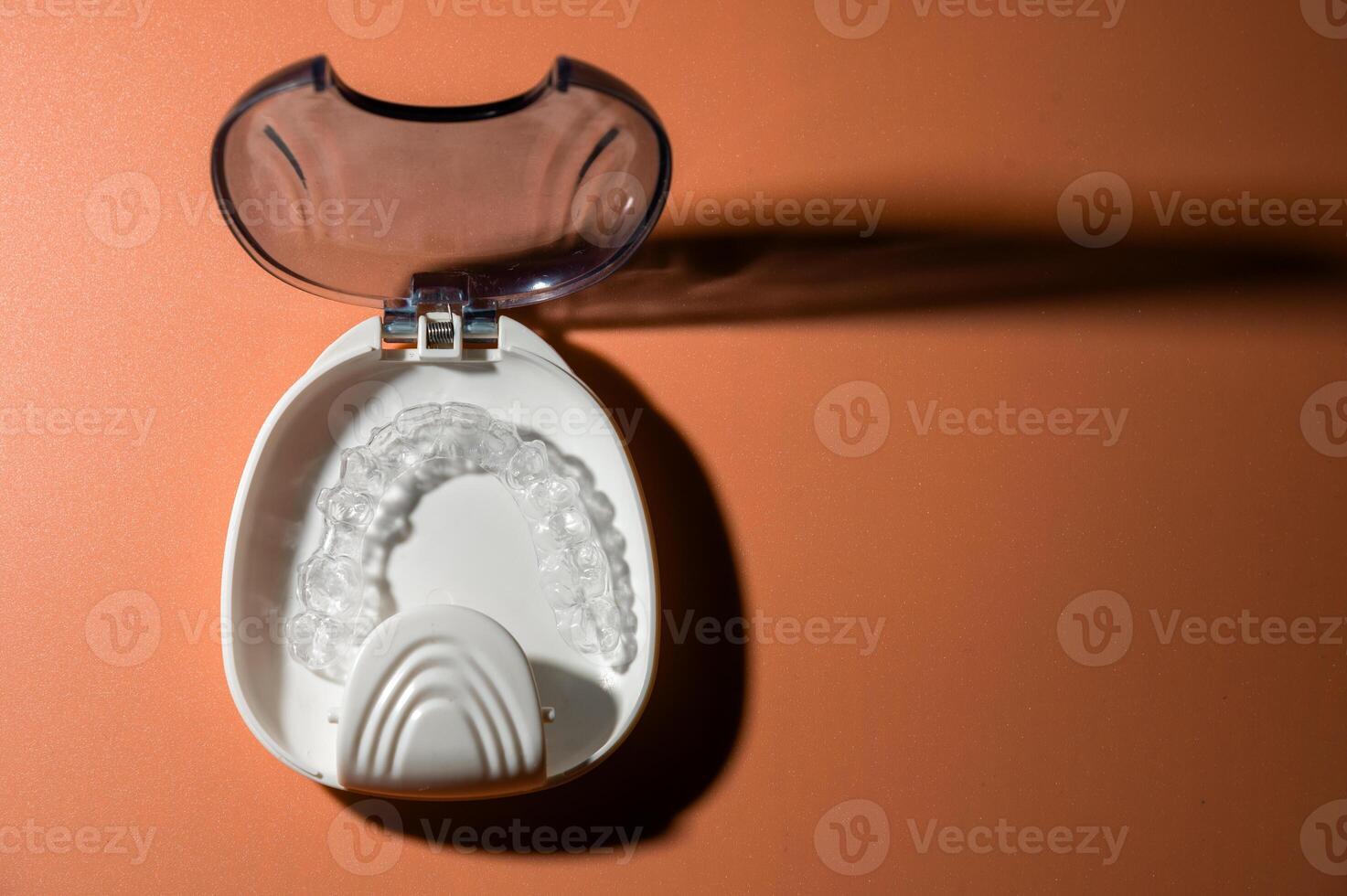 White plastic case with transparent brackets on a peach background. Invisible removable retainers for orthodontic treatment photo