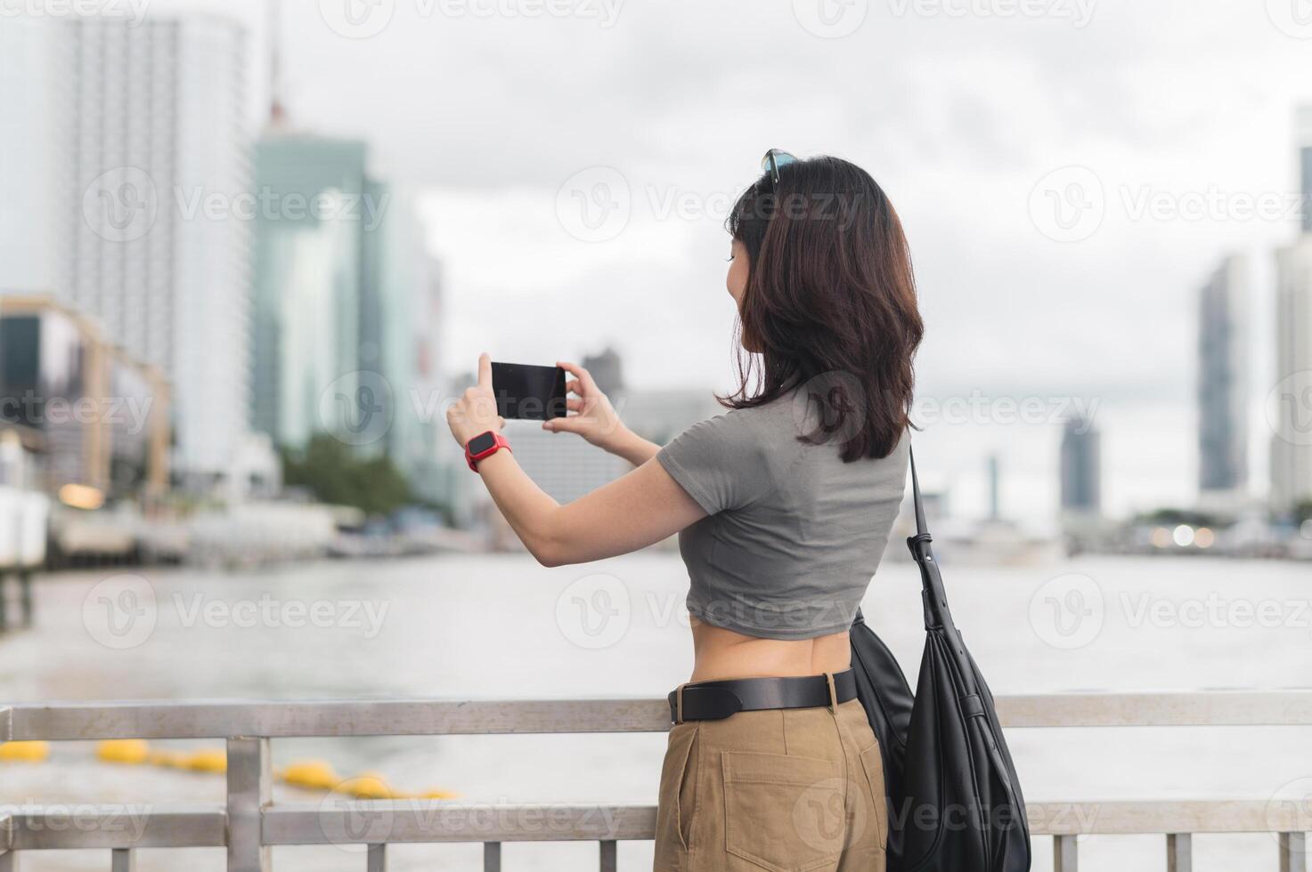 Solo southeast asian woman teenager blogger take photo with smartphone and wait for boat. An express world travel explorer tourism concept for local cultural experience Chao Phraya river Bangkok