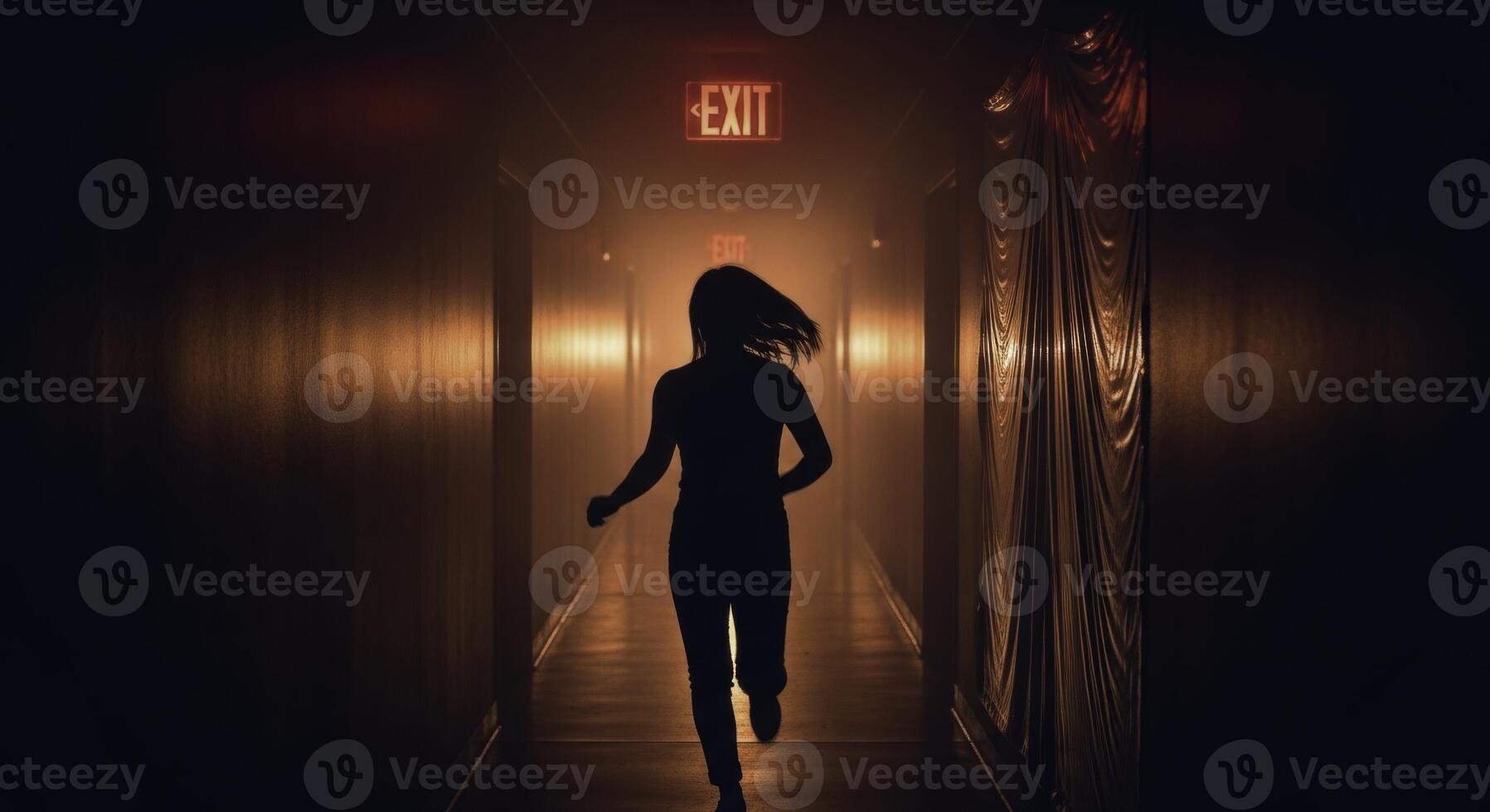 Dramatic silhouette of a woman running towards a glowing red exit sign in a dark hallway photo
