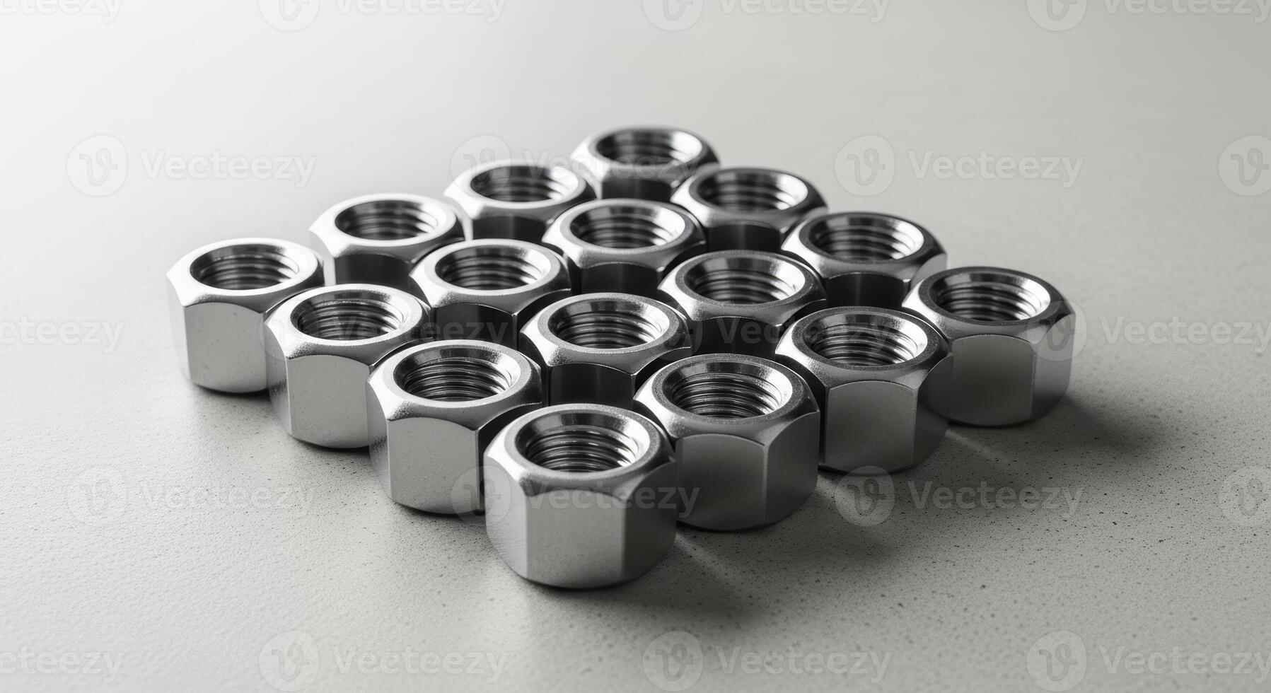 Neatly arranged group of shiny metal hexagonal nuts on a light grey surface photo