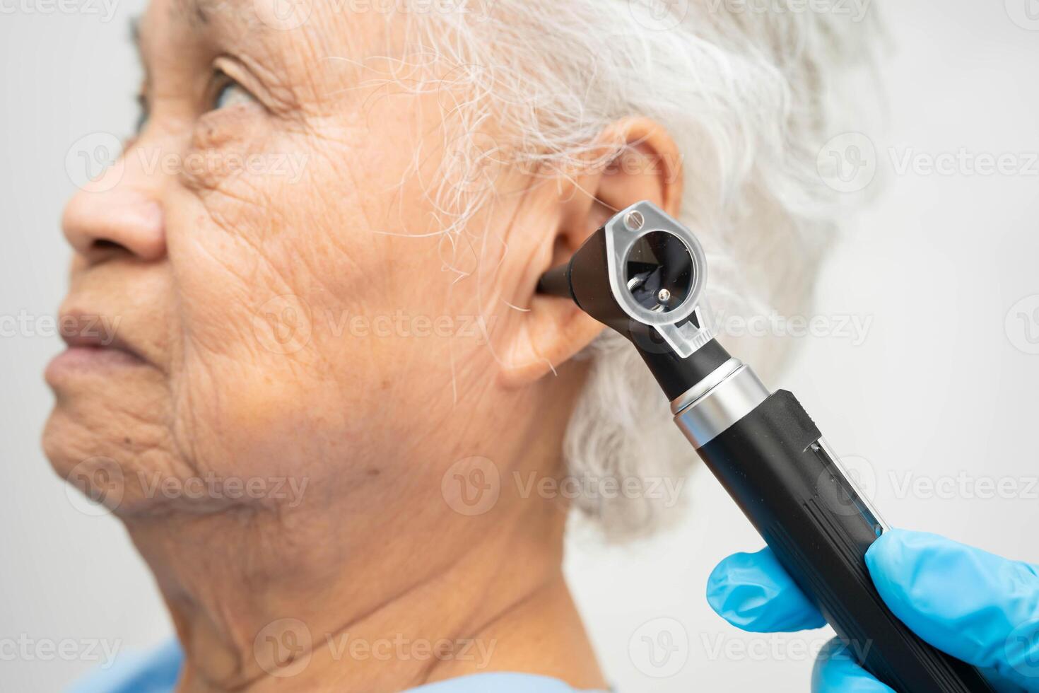 Otolaryngologist ENT physician doctor examining senior patient ear with otoscope hearing loss problem. photo