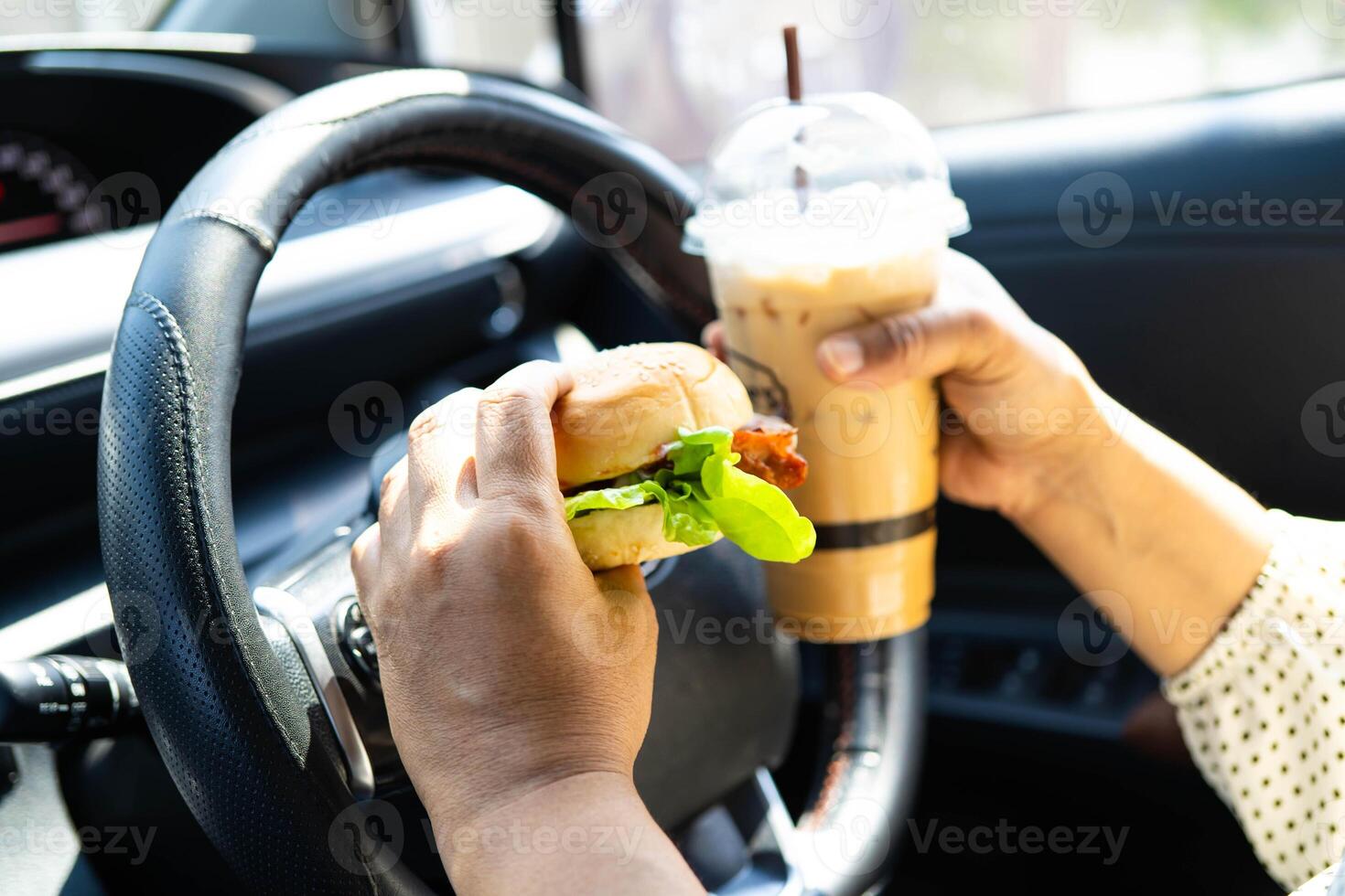 Asian woman driver hold and eat hamburger and cold coffee in car. photo