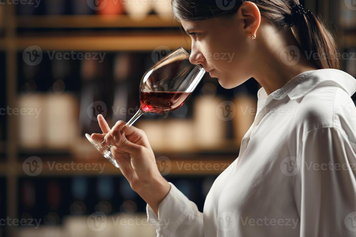 Close up profile portrait of professional woman sommelier in wine cellar degustation red wine in glass, smelling and analyzing. photo