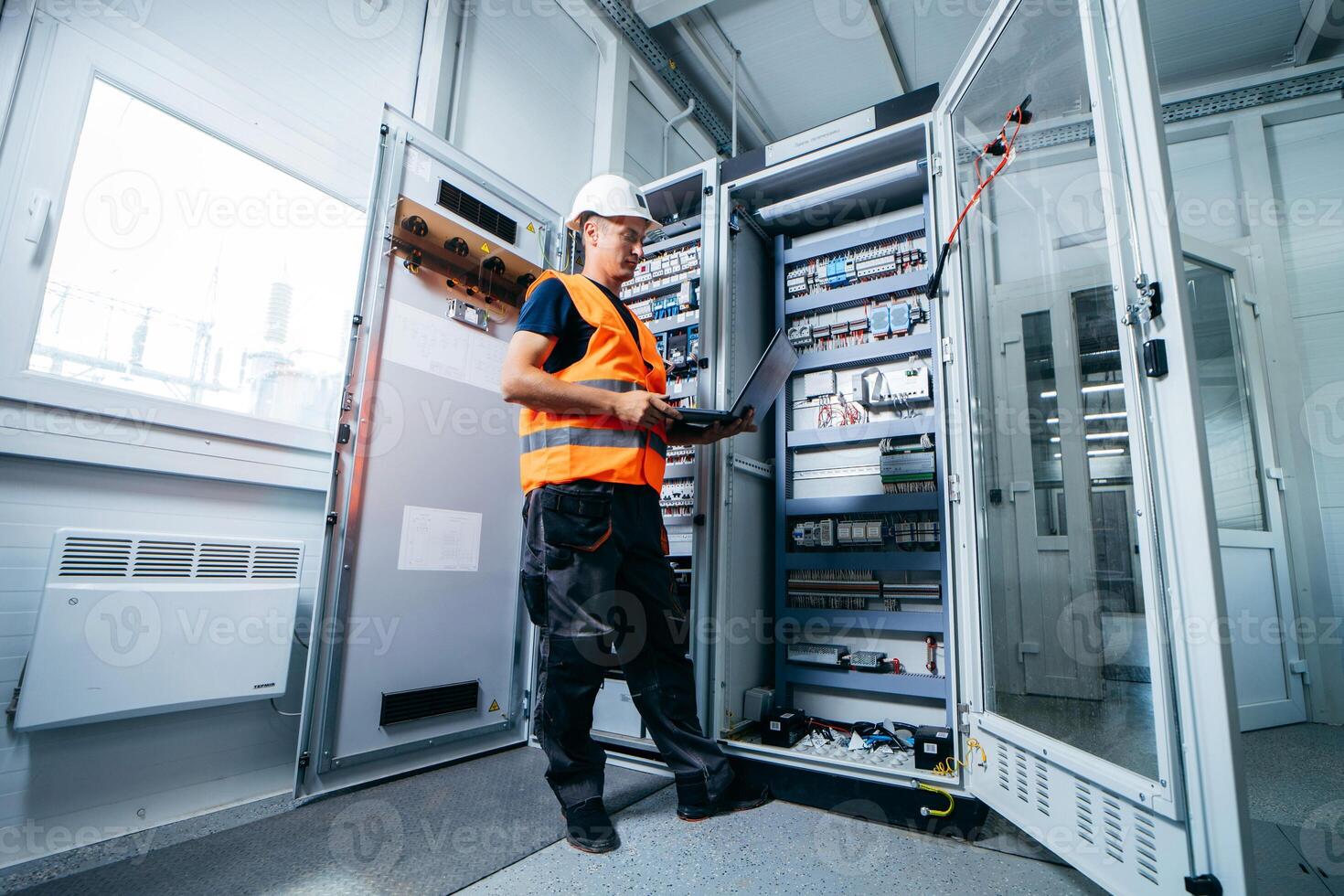 Adult electrician builder engineer testing and screwing equipment in fuse box and repairing of electricity power station photo