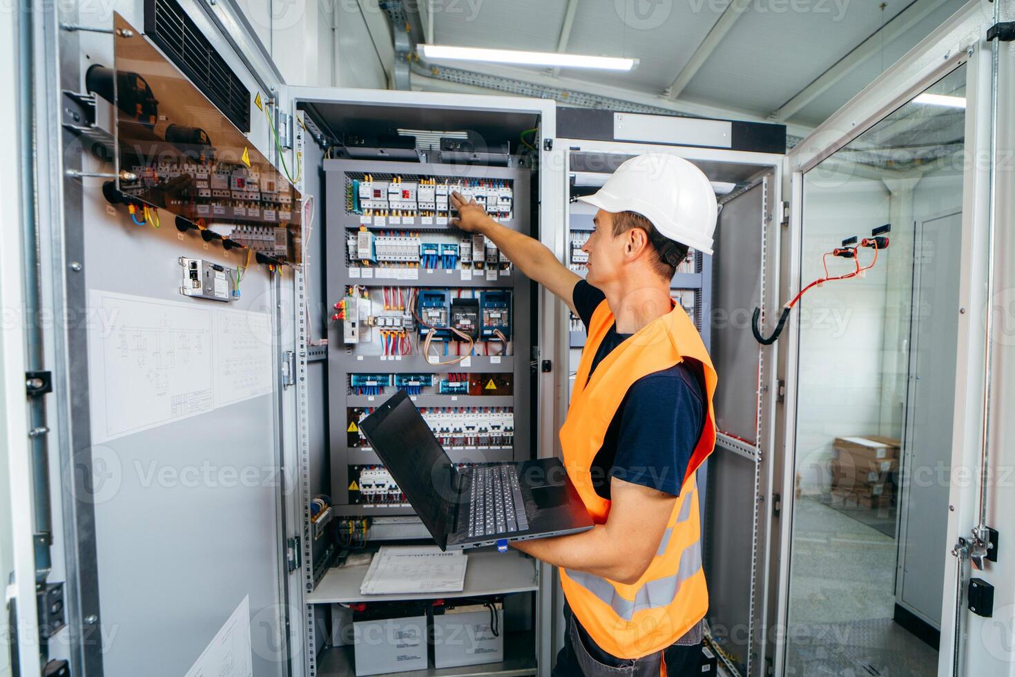 Adult electrician builder engineer testing and screwing equipment in fuse box and repairing of modern electricity power station. Automatic control cabinet. photo
