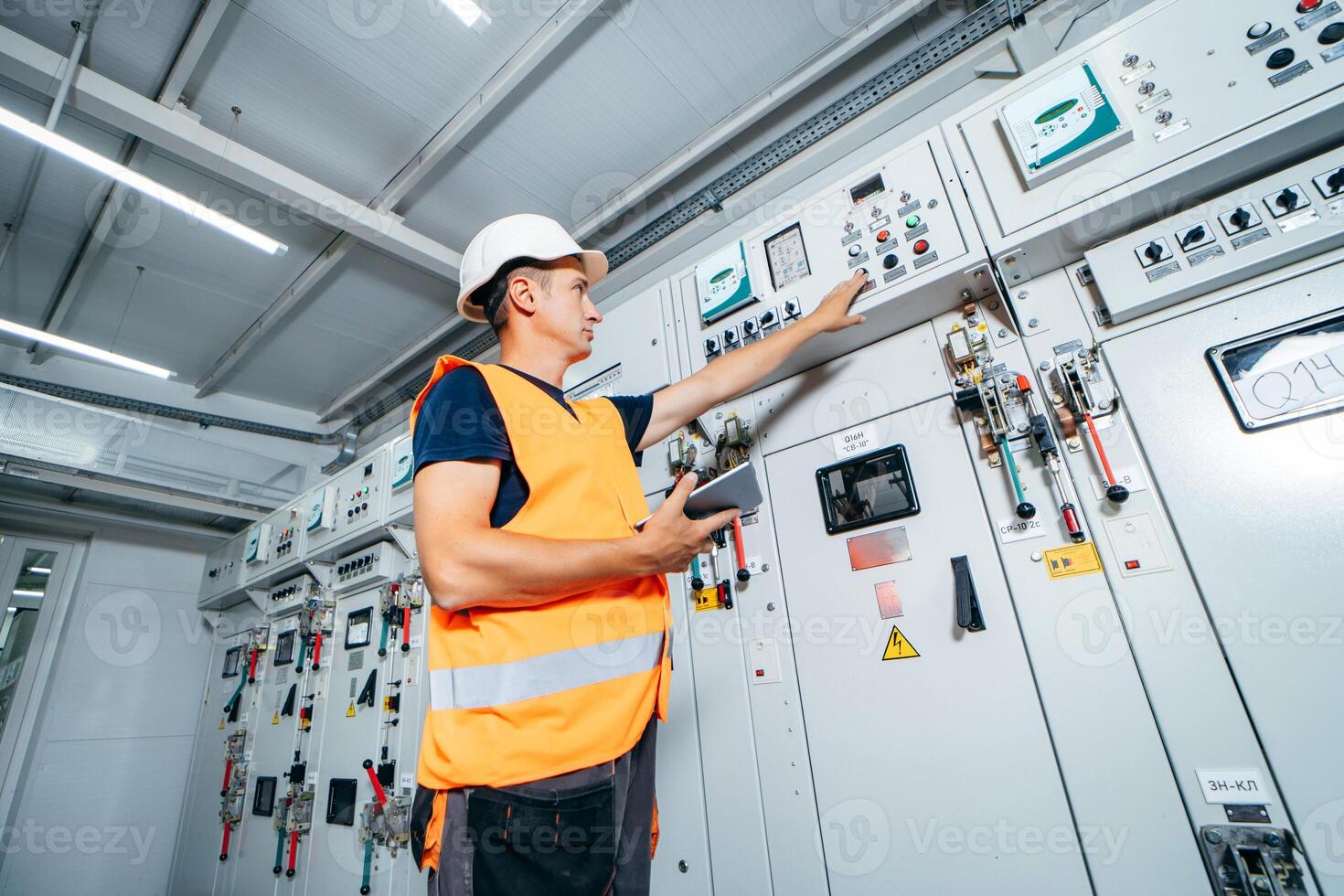 Adult electrician builder engineer testing and screwing equipment in fuse box and repairing modern electricity power station using data from the tablet. Automatic control cabinet photo