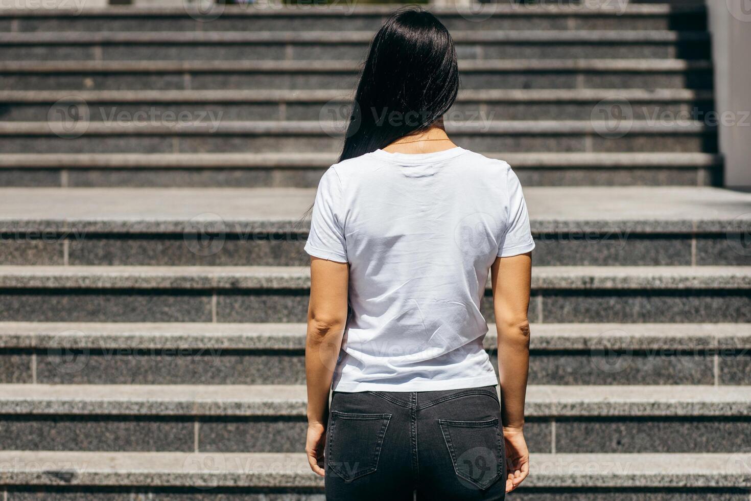 Stylish asian girl wearing white t-shirt and glasses posing against street , urban clothing style. Back view photo