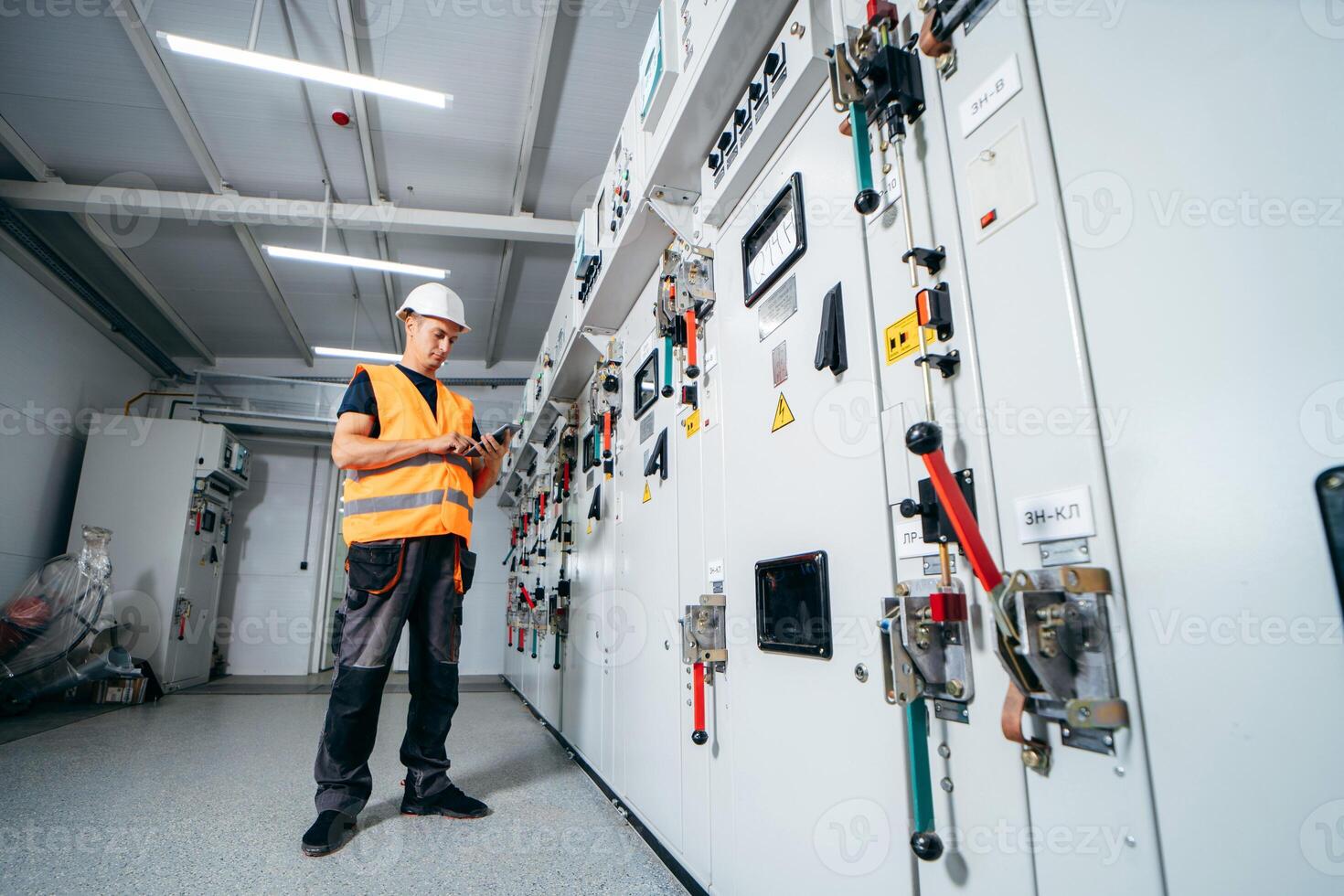 Adult electrician builder engineer testing and screwing equipment in fuse box and repairing modern electricity power station using data from the tablet. photo