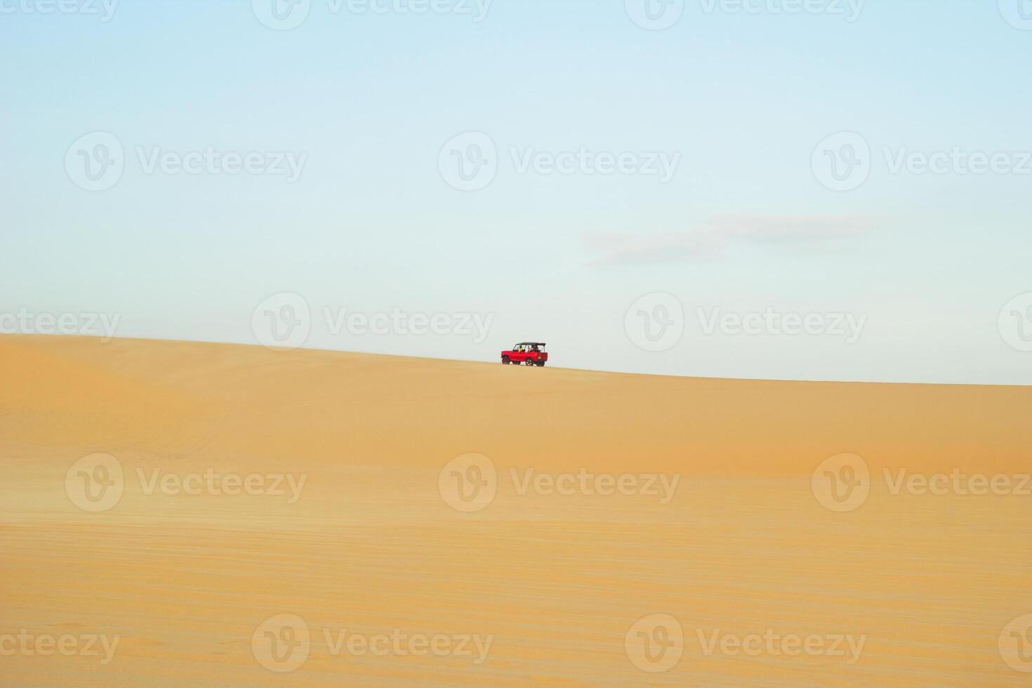 Red Vehicle Driving Across Arid Desert Landscape Under Pale Sky. Mui Ne, Vietnam, White Dunes. photo