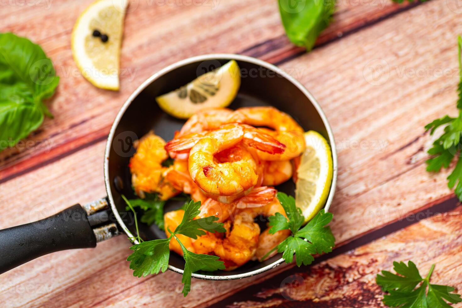 Juicy fried shrimps with lemon wedges in a frying pan on a wooden photo