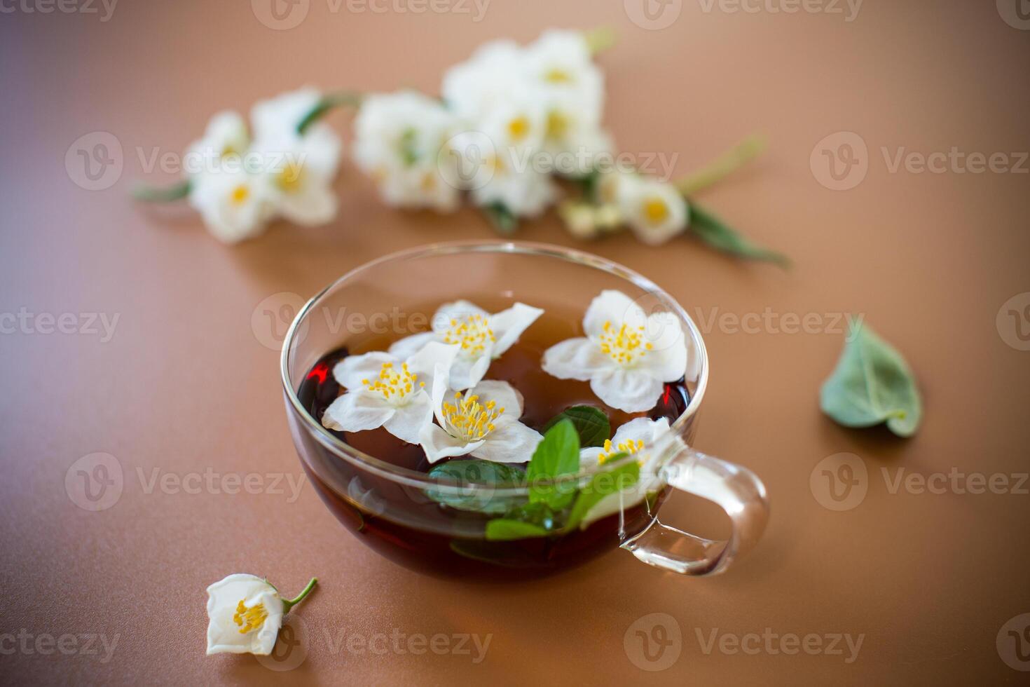 Glass teapot with jasmine and green tea isolated on a brown background photo