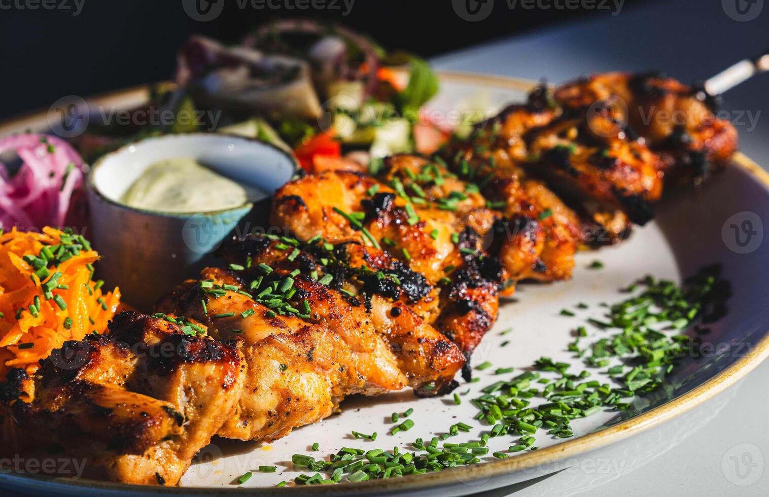 Grilled chicken skewers with fresh salad and sauce on plate photo