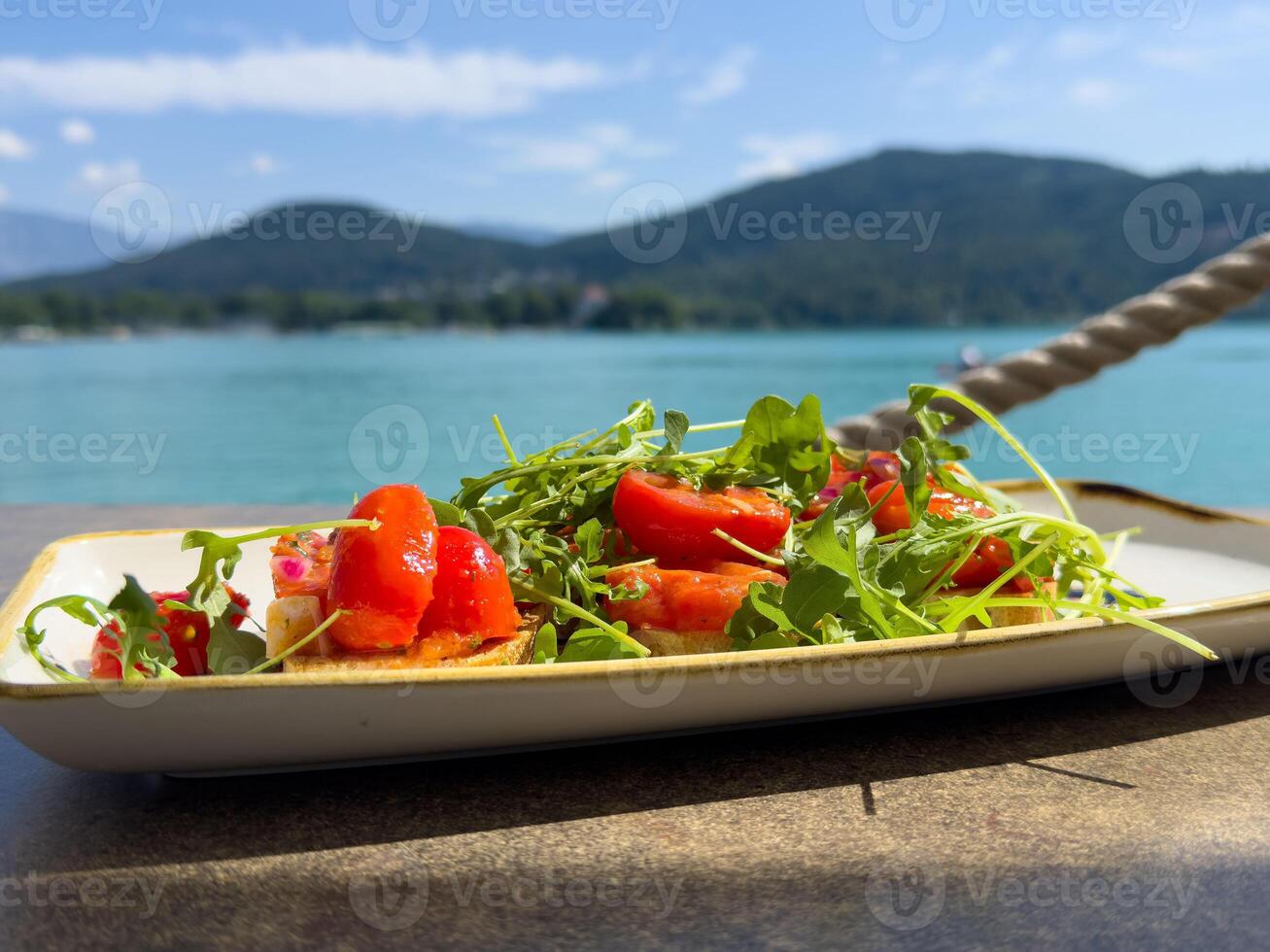Fresh summer salad with arugula, cherry tomatoes, and feta by a scenic lake view photo