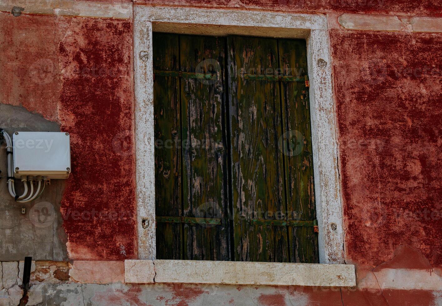 Rustic aged window with weathered green shutters on red textured wall photo