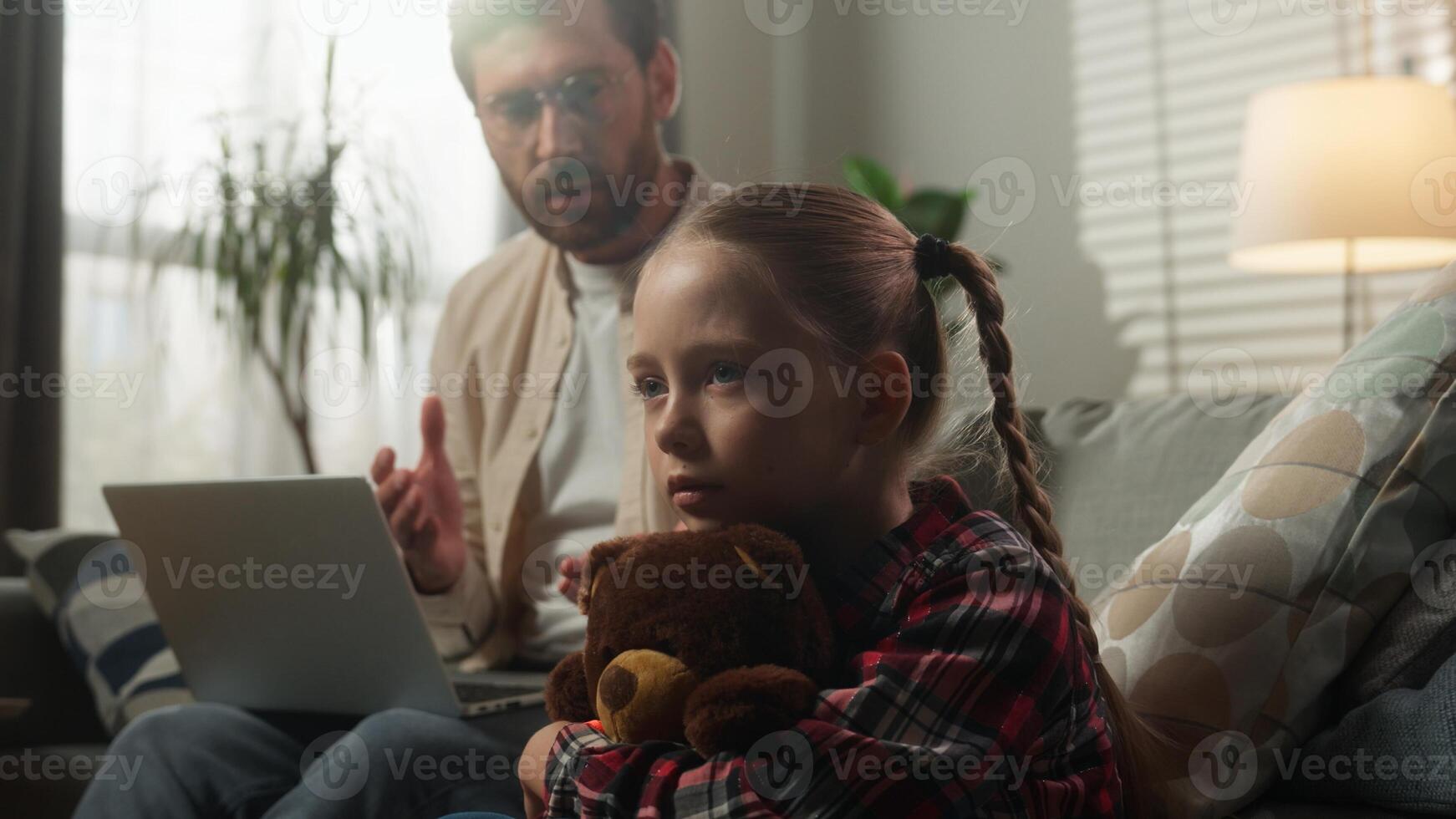 Caucasian family at home remote working dad using computer on sofa speaking to sad little girl child kid cuddling Teddy Bear conflict emotional stress childhood problem loneliness attention deficit photo