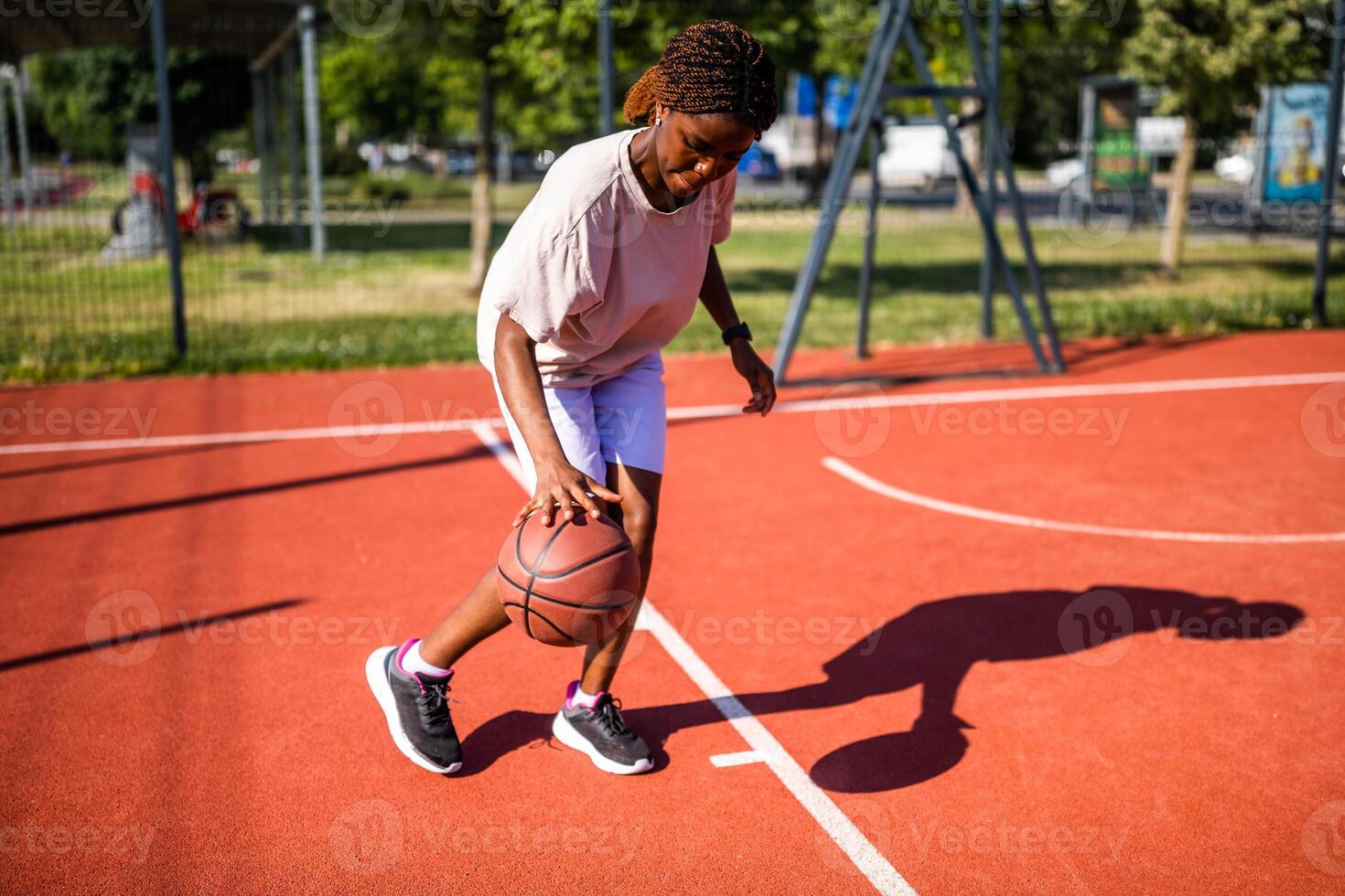 A focused female athlete practices dribbling and ball control on a basketball court under the bright summer sun, enjoying the sport and urban environment. photo