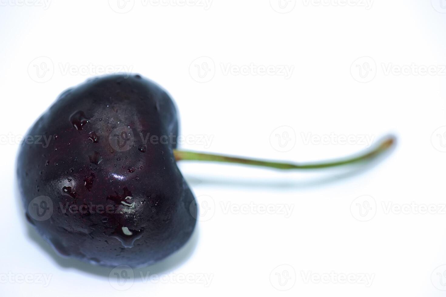 Close up view of a fresh black cherry with gleaming droplets on a clean white surface photo