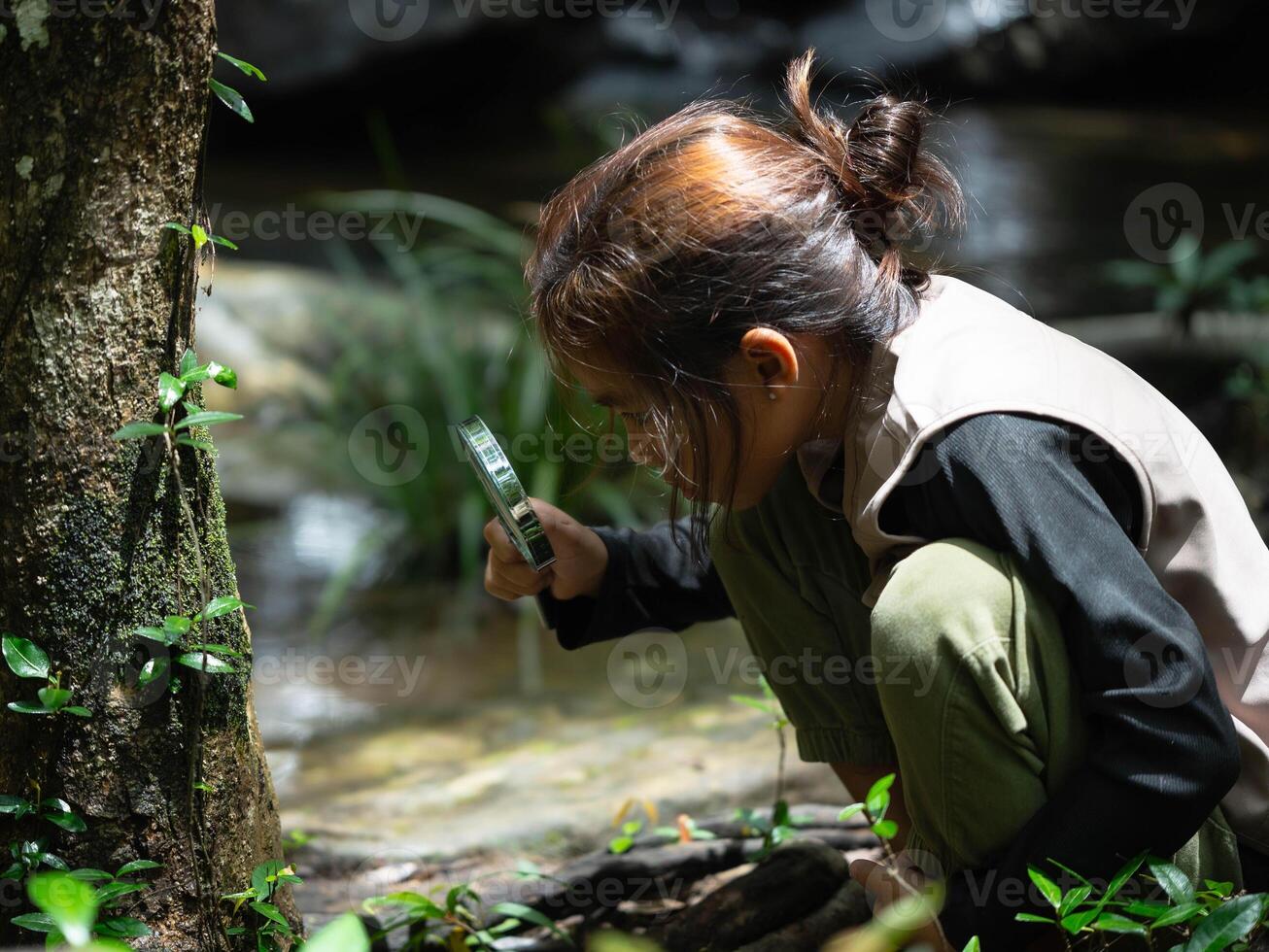 Happy little girl is exploring in the forest and looking for insects with a magnifying glass. Adventure tourism and learning concept photo