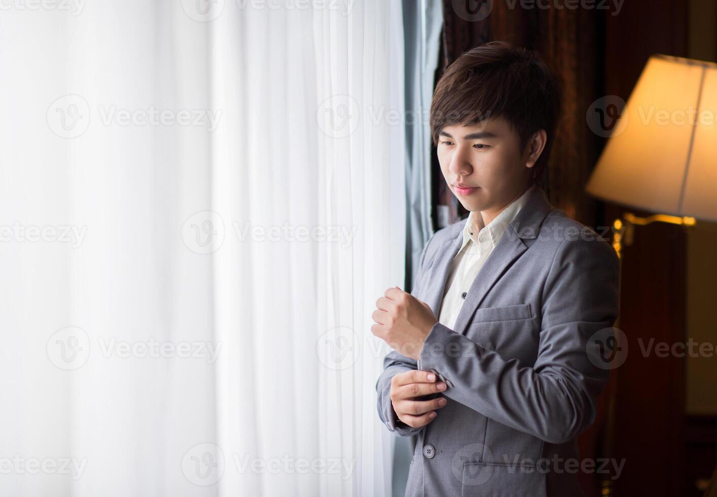 The younng asian businessman is standing nearby the window with white curtain. photo