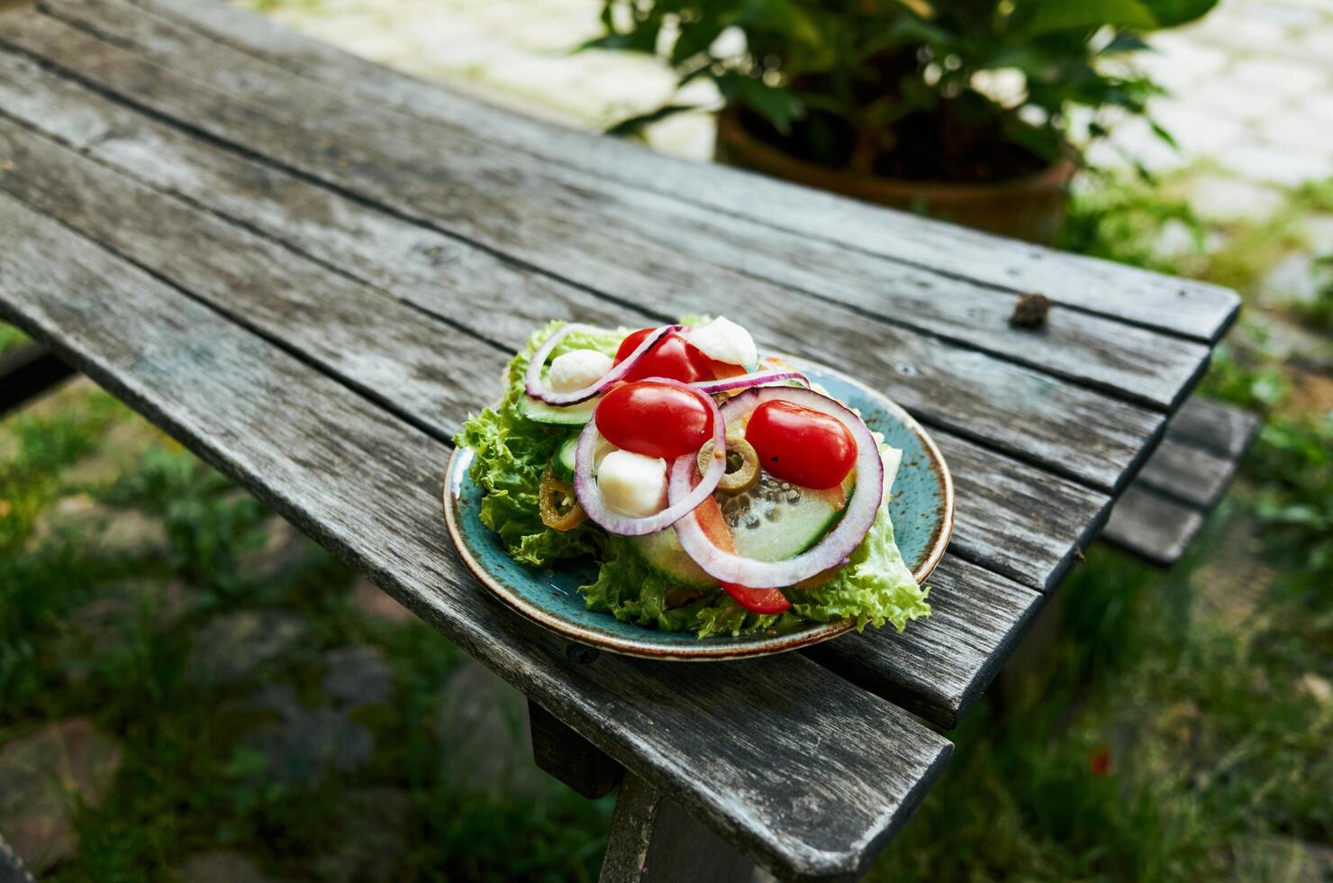 Plate of salad with lettuce, tomatoes, and onions sits on a wooden table photo