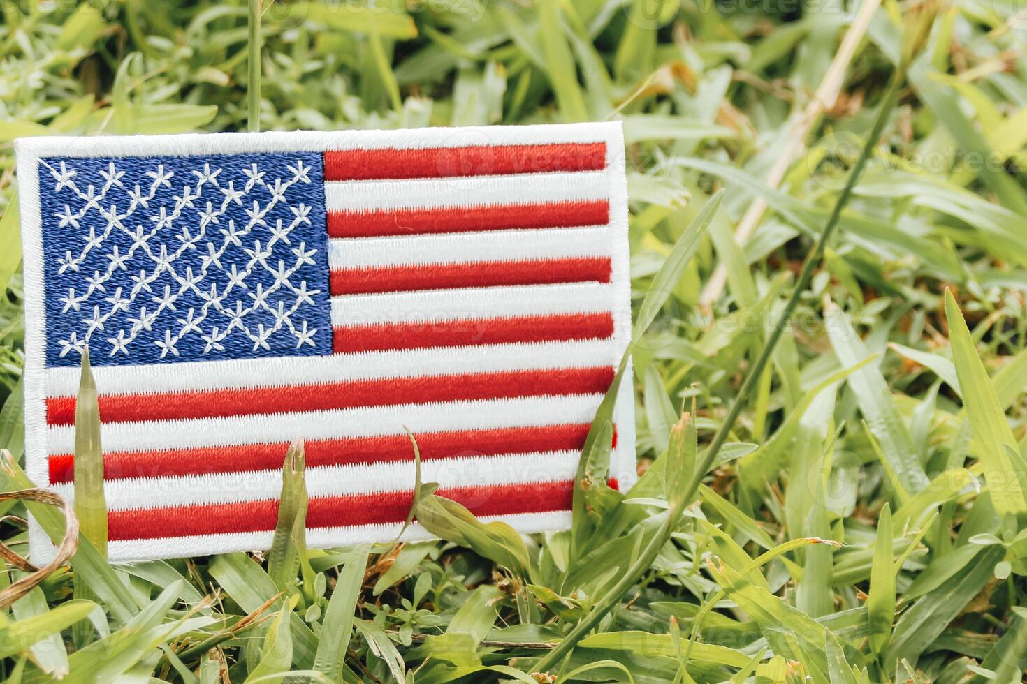 Horizontal eco friendly USA flag crafted from fabric and thread, placed on grass under warm natural light. Surrounded by leaves, symbolizing Earth Day and climate harmony in North America. photo