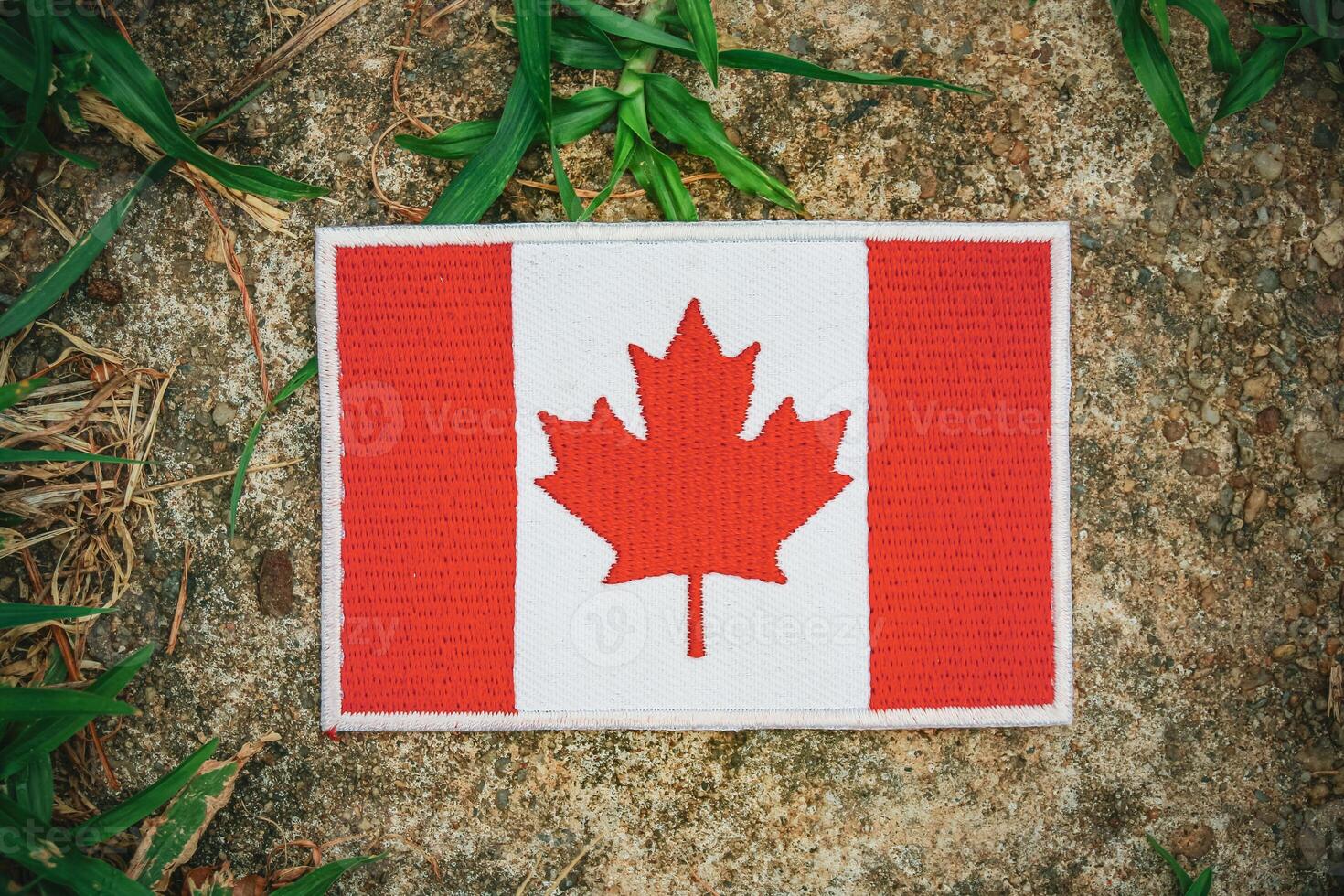 Top view of eco friendly embroidered Canadian flag on old stone, with green grass and leaves around. Natural calmness and sustainable design. photo