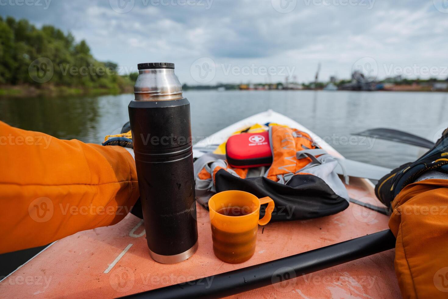 A person is sitting comfortably on a kayak that is floating on the water, holding a thermos in one hand and a steaming cup of coffee in the other, enjoying the serene surroundings photo