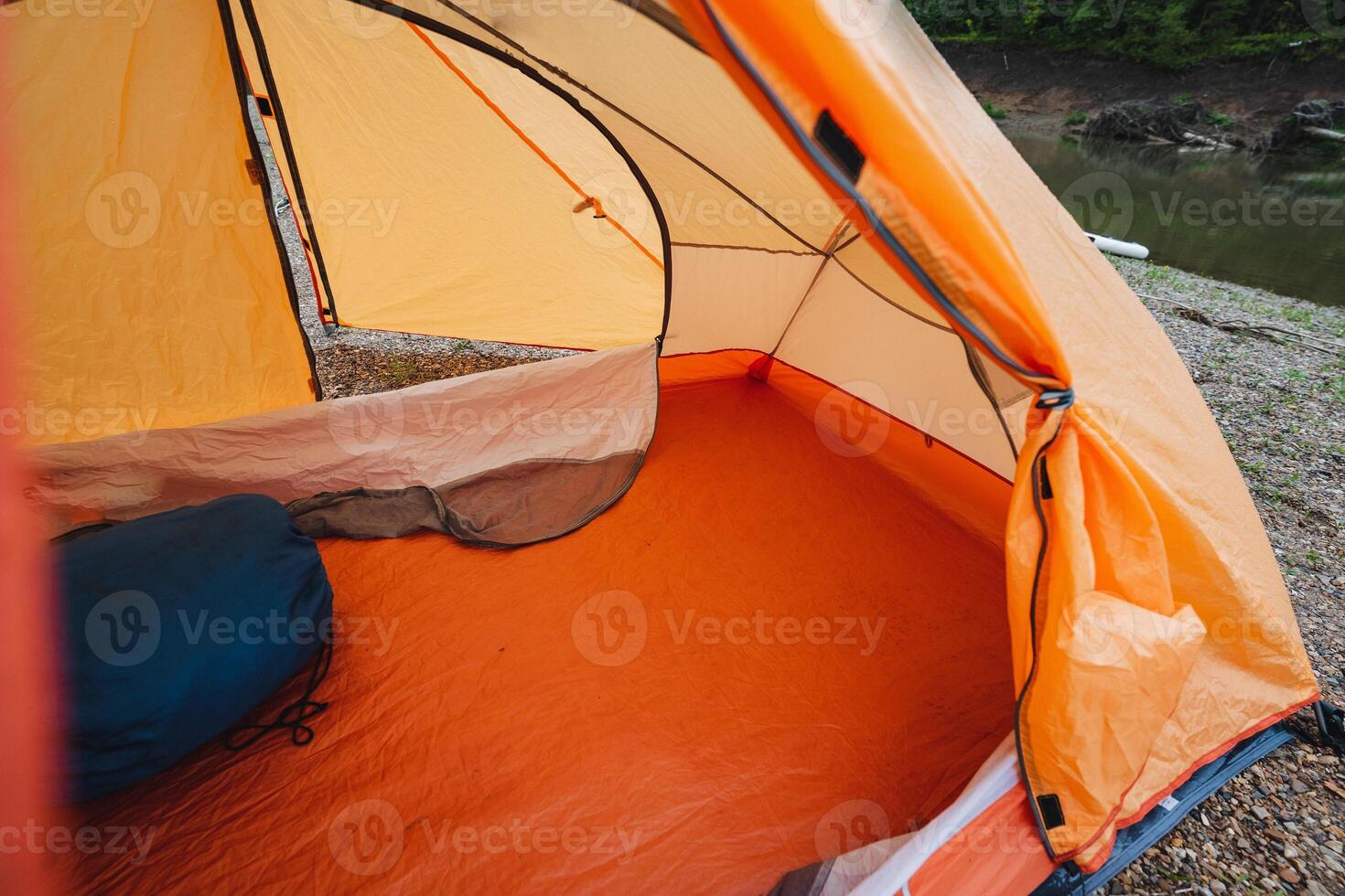 A bright orange tent is set up on the soft, inviting ground beside a gently flowing river, creating a stunning and picturesque camping scene in the beautiful and serene outdoors photo