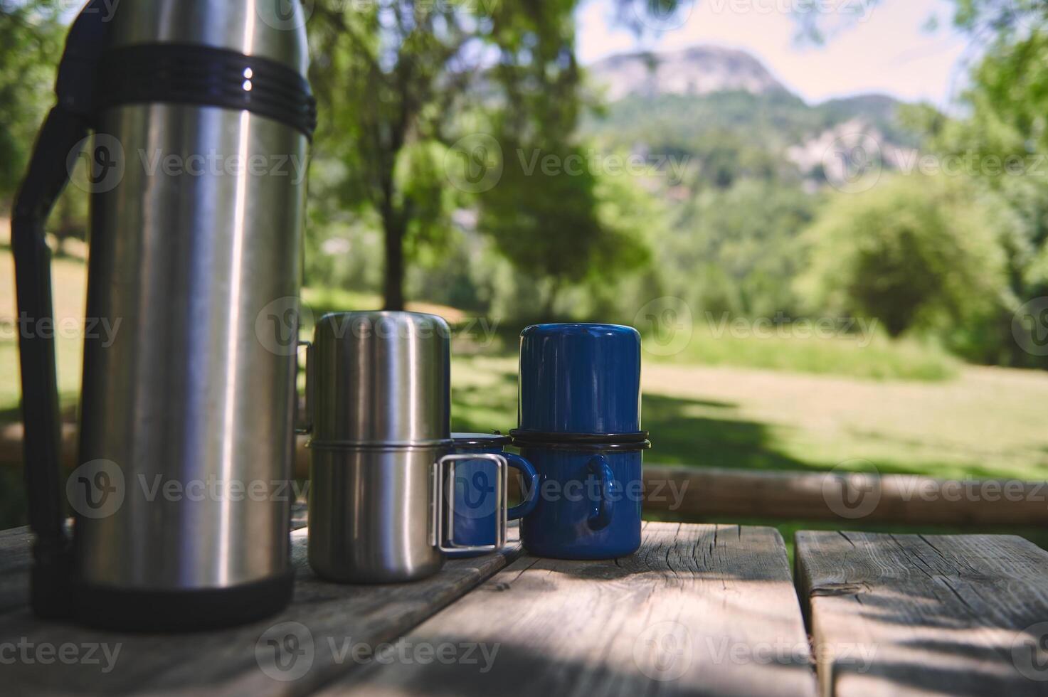 Thermos and Cups Placed on a Wooden Table with Scenic Forest View photo
