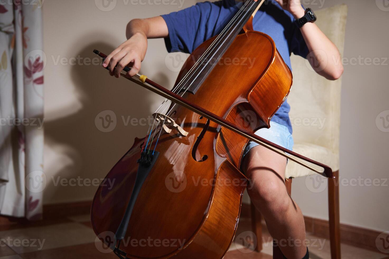 Individual playing cello with precision and emotion, showcasing the artistry of string instrument mastery in an indoor setting. Light accents enhance the polished wooden finish of the cello. photo