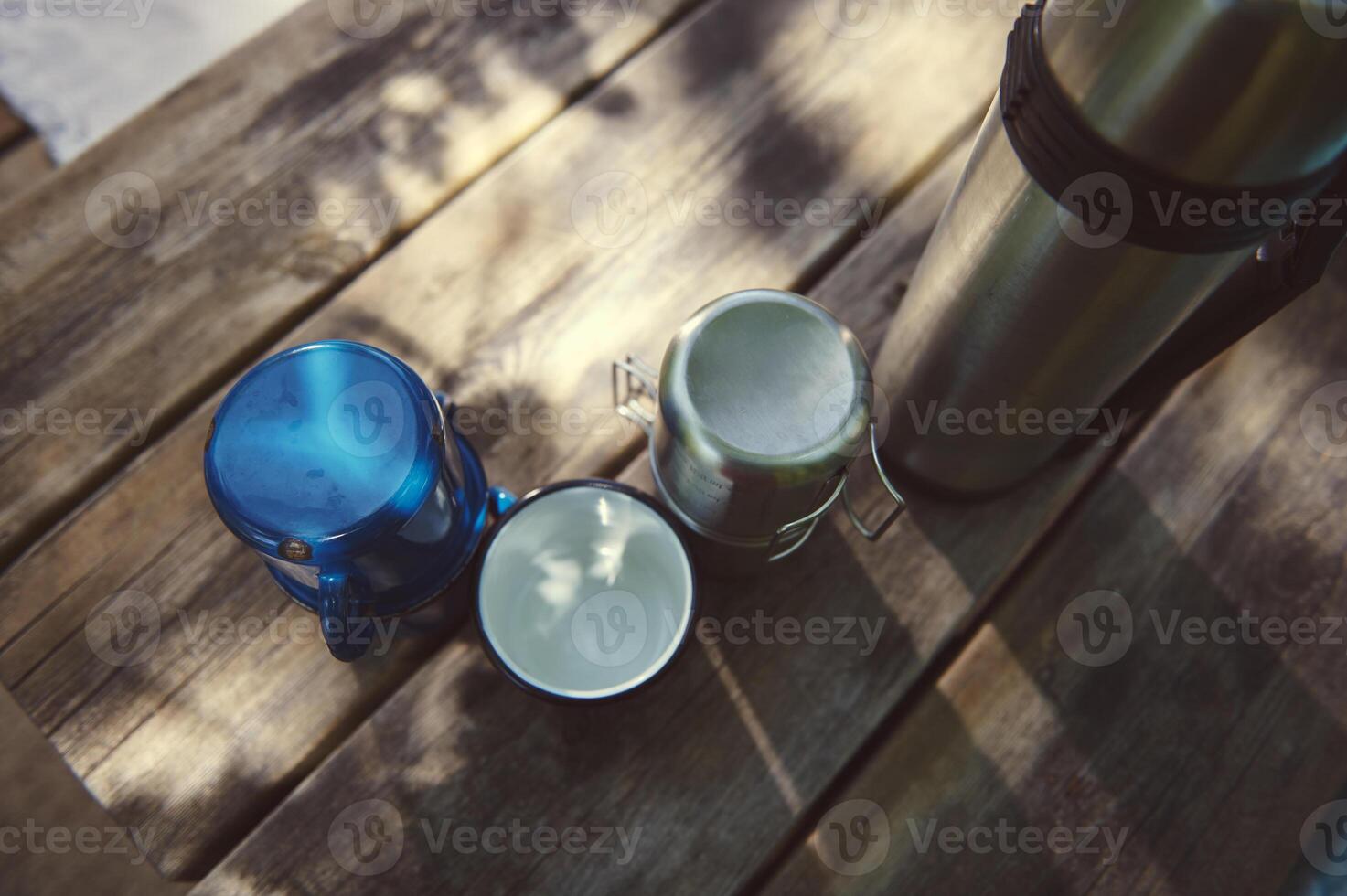 Camping Setup with Thermos and Mugs on Wooden Table Outdoors photo