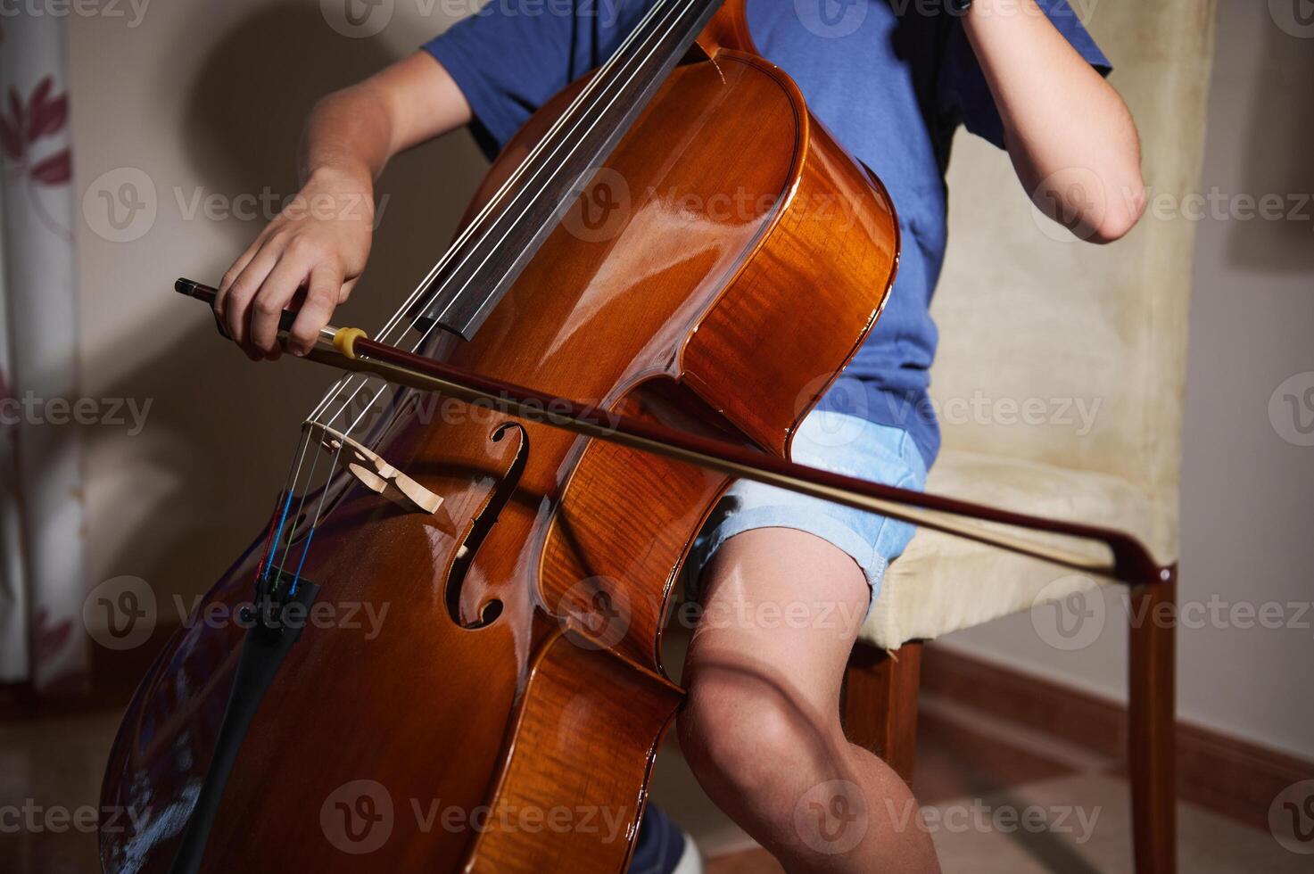 A focused young musician skillfully playing a cello indoors, emphasizing the beauty and craftsmanship of the musical instrument against a cozy and intimate setting. photo