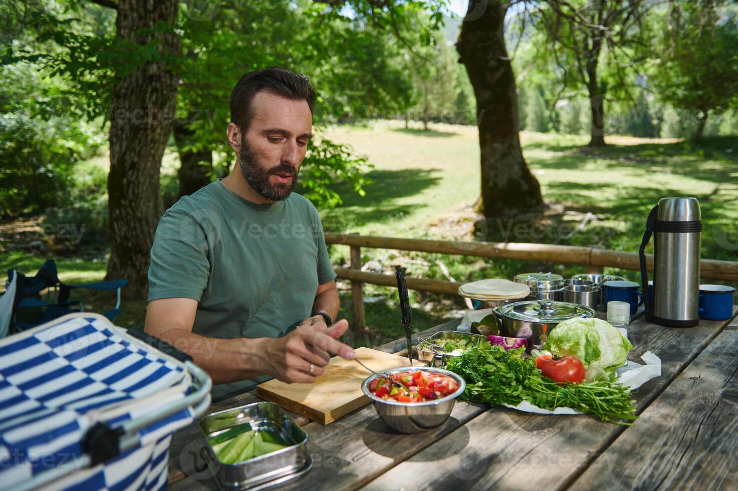 Man Preparing a Healthy Salad Outdoors at a Picnic Table Surrounded by Nature photo