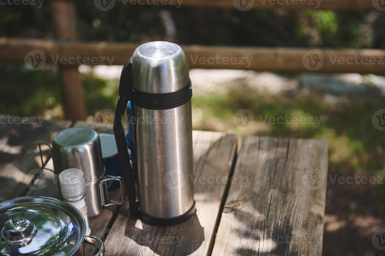 Thermos and Various Table Items on a Wooden Outdoor Picnic Table in Nature photo