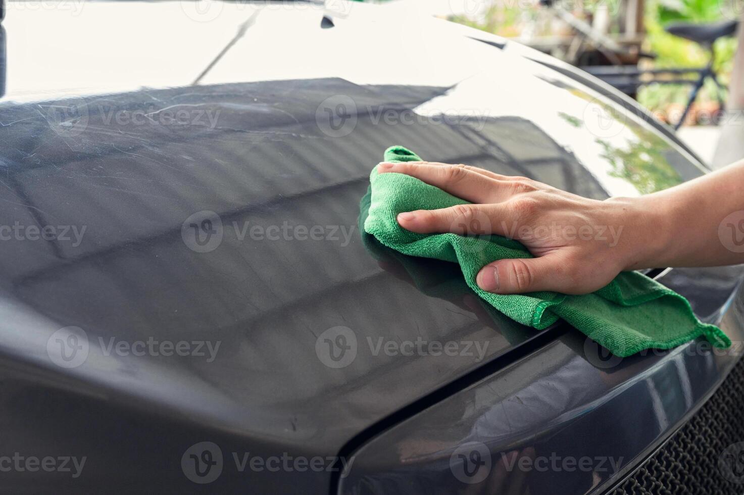 Man cleaning car with green microfiber cloth on hood photo