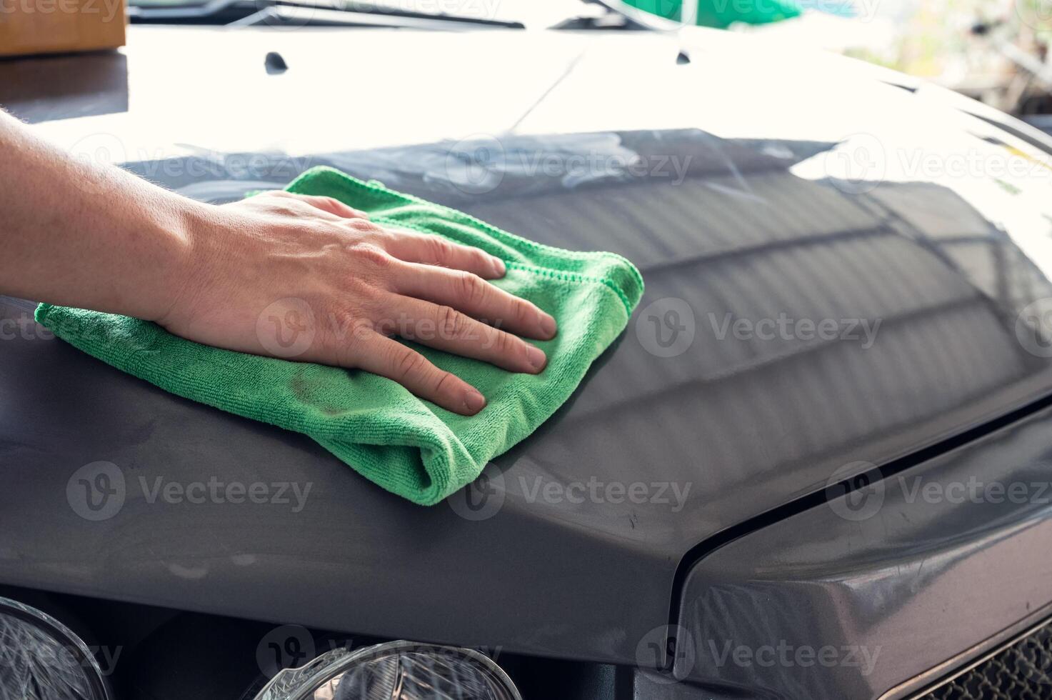 Male hand wiping the stain with microfiber on car hood photo