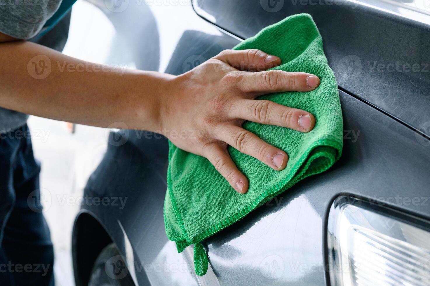 Man cleaning grey car with green microfiber cloth on hood photo