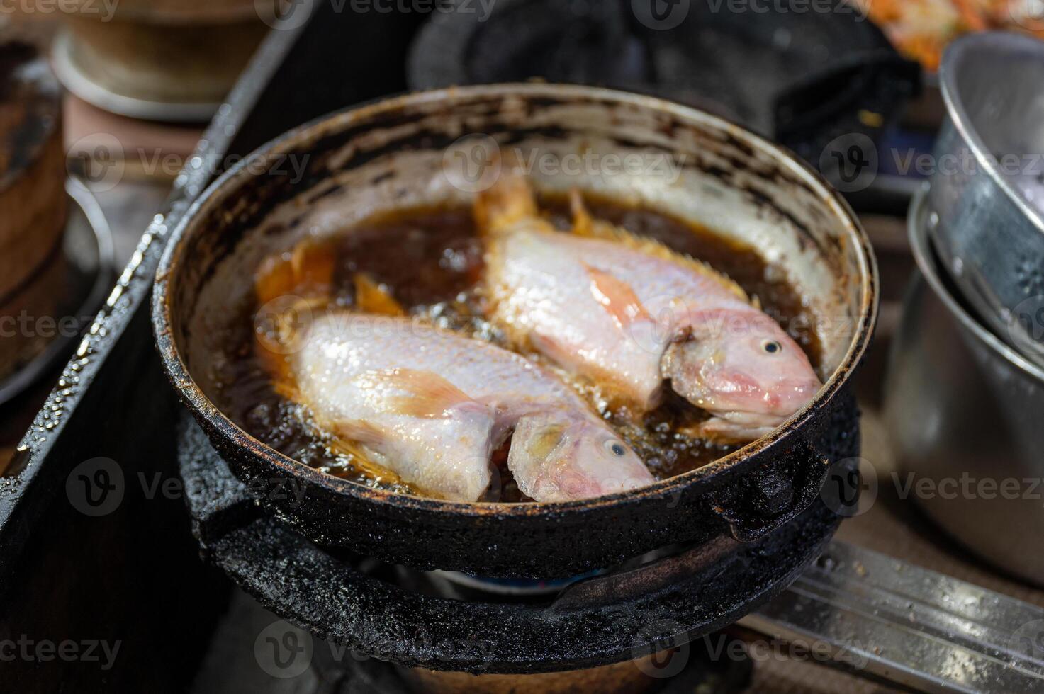 Two red tilapia fish frying with bubbling in dirty pan photo