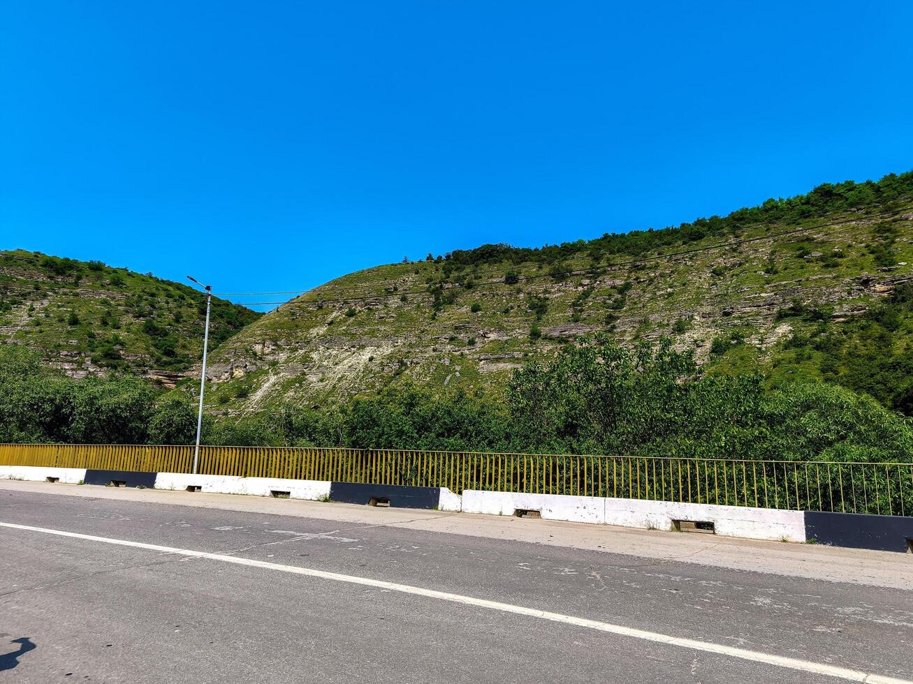 A road with a yellow and black fence on the side. The road is empty and the sky is blue photo