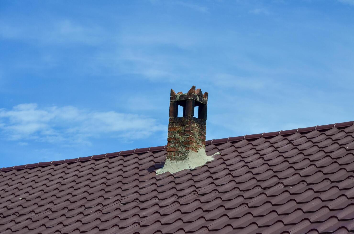A chimney on a roof with a blue sky in the background. The chimney is covered in rust and has a small hole in it photo