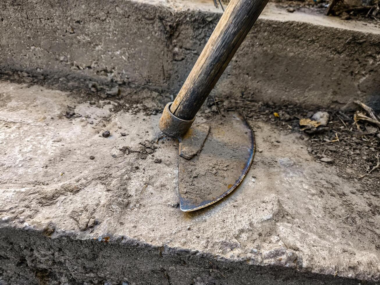 A shovel is leaning against a concrete wall. The shovel is old and rusted. The image has a mood of weariness and abandonment photo